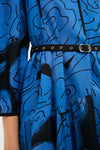 Close-up of the LOVEBIRDS Eden Dress, an A-line blue piece with black abstract patterns, a black belt with silver eyelets and buckle, and a gathered waist detail.