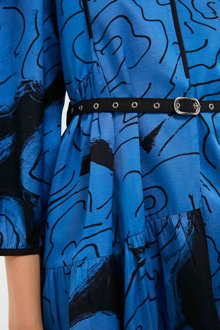 Close-up of the LOVEBIRDS Eden Dress, an A-line blue piece with black abstract patterns, a black belt with silver eyelets and buckle, and a gathered waist detail.