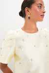 Woman in a classic, pale yellow Ivory Olivia Top with pearl and rhinestone embellishments, embodying effortless glamour, paired with chic dropped earrings, exuding a high-end, fun style.