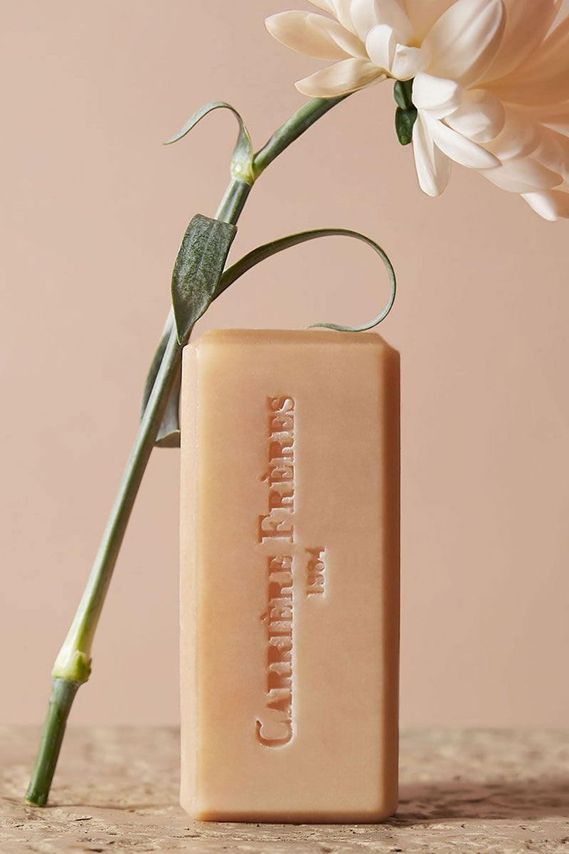 Florae Solid Body Soap—a classic, high-end peachy-beige bar embossed with a logo, paired with a creamy flower, exuding effortless floral and citrus elegance.