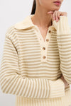 A person wearing a cream and beige Striped Doro Henley Sweater by Ciao Lucia, featuring a rib-knit collar and button placket, rests their chin on their hand.