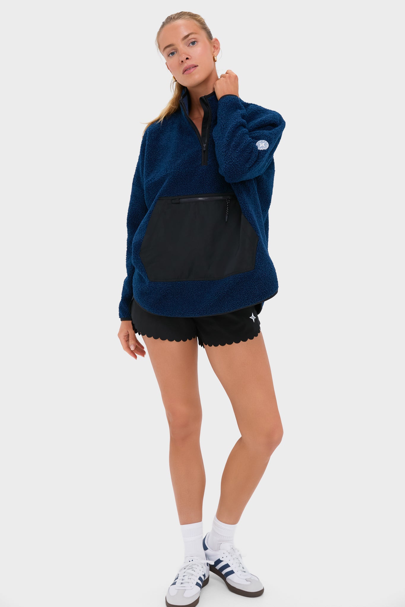 Young woman models the Navy Fleece Cady Quarter Zip, featuring a classic quarter-zip design and kangaroo pocket, paired with black shorts for an effortless, high-end sporty look.