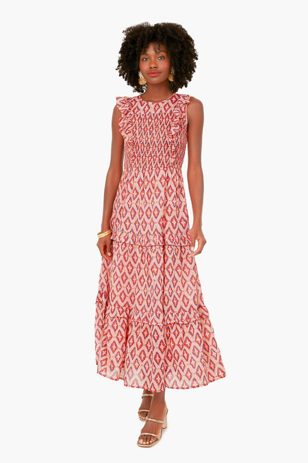 Woman wearing the Banjanan Surreal Dream Dolce Iris Dress—an ankle-length organic cotton dress with red geometric patterns, ruffled shoulders, handmade embroidery on a smocked bodice—paired with heeled sandals.