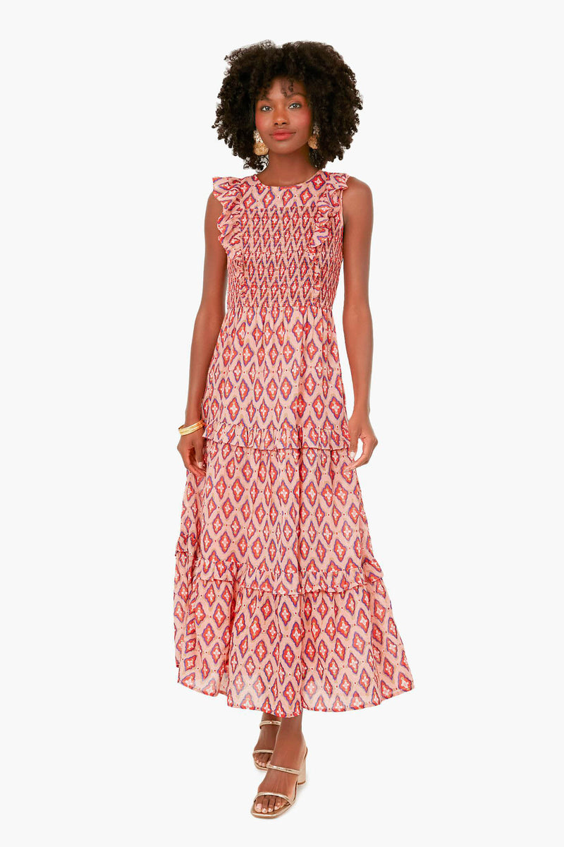 Woman wearing the Banjanan Surreal Dream Dolce Iris Dress—an ankle-length organic cotton dress with red geometric patterns, ruffled shoulders, handmade embroidery on a smocked bodice—paired with heeled sandals.