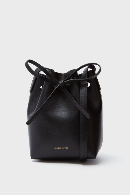 A black Mansur Gavriel Mini Mini Bucket Bag made from Italian Saffiano leather, featuring a drawstring closure and gold-embossed branding near the bottom.