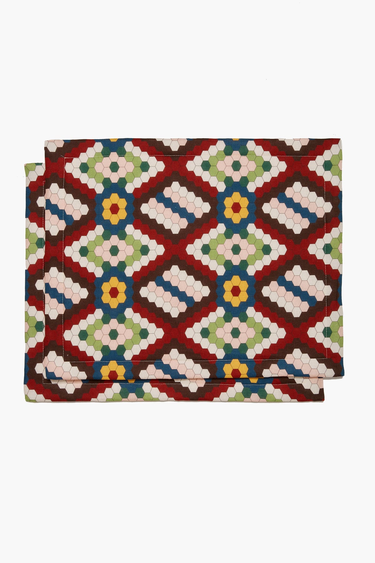 Two folded La DoubleJ fabric napkins with a geometric hexagonal pattern in red, green, blue, yellow, and white add vibrant style to your Italian linen placemats for a colorful table setting.