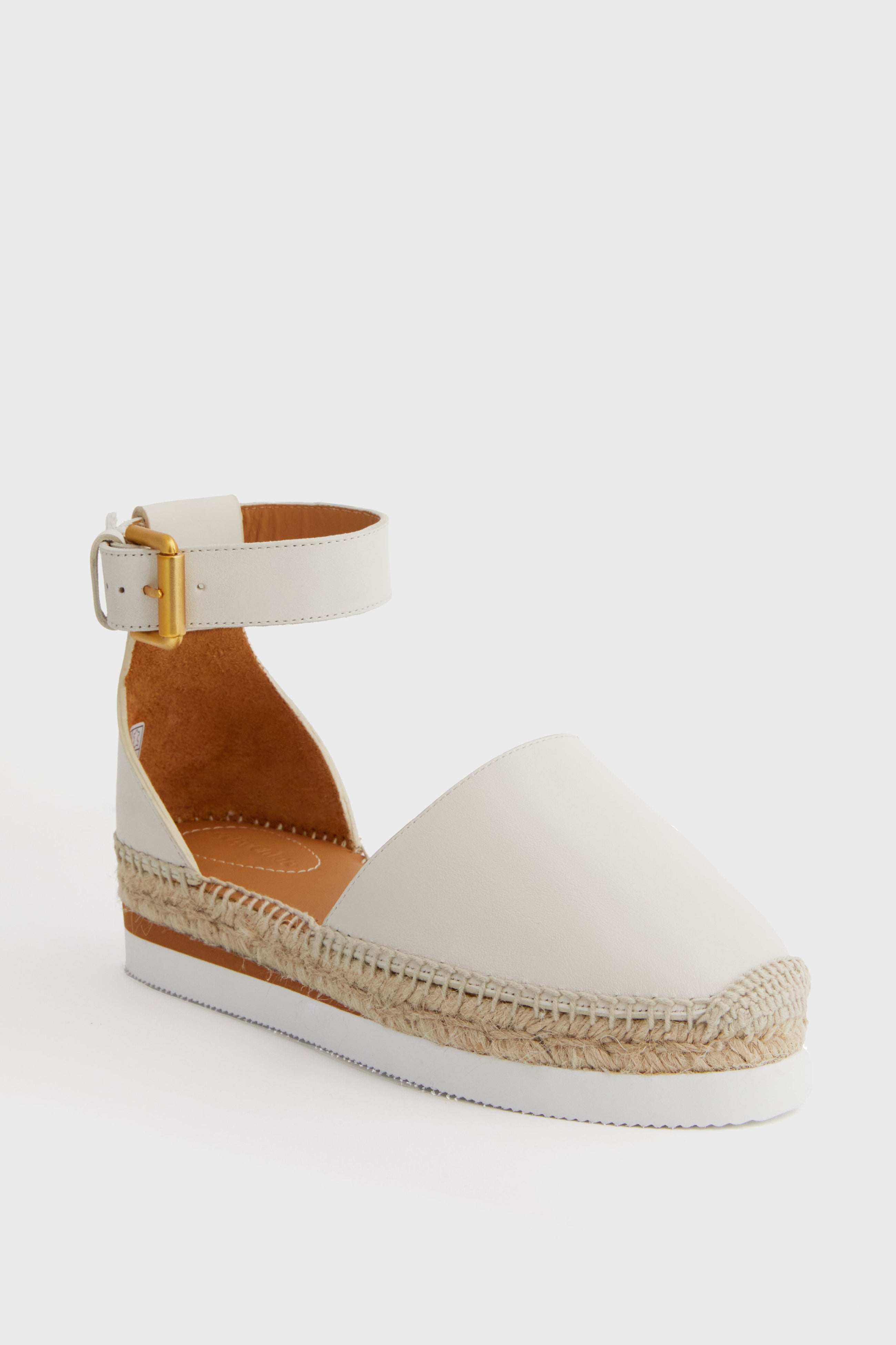 A white closed-toe espadrille sandal by See by Chloe, featuring an ankle strap, jute-wrapped platform sole, and gold buckle—ideal for fans of classic braided jute sandals.