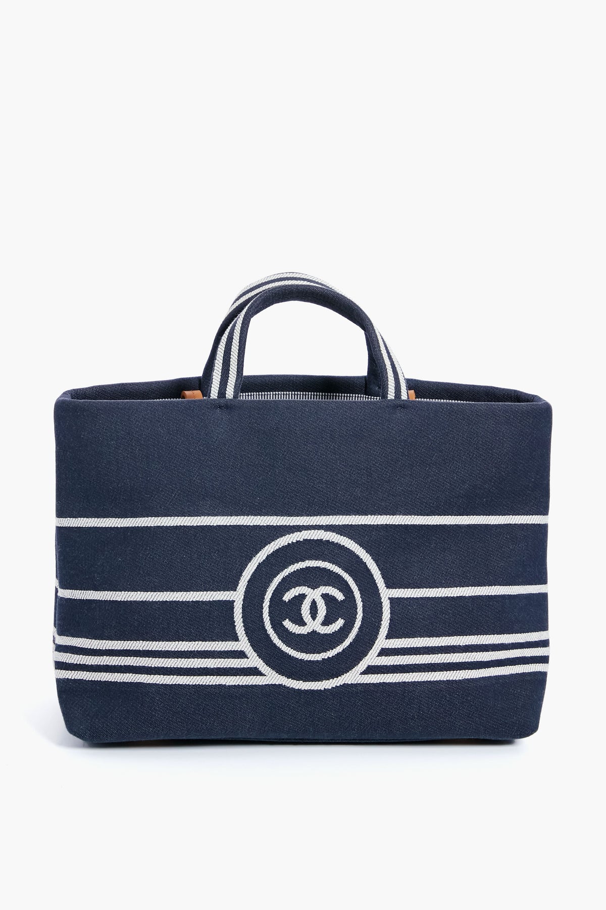 A navy blue luxury handbag with white horizontal stripes, two short handles, and a bold front logo from the Tuckernuck Archive Collection, inspired by the Chanel Denim Canvas Border Tote.