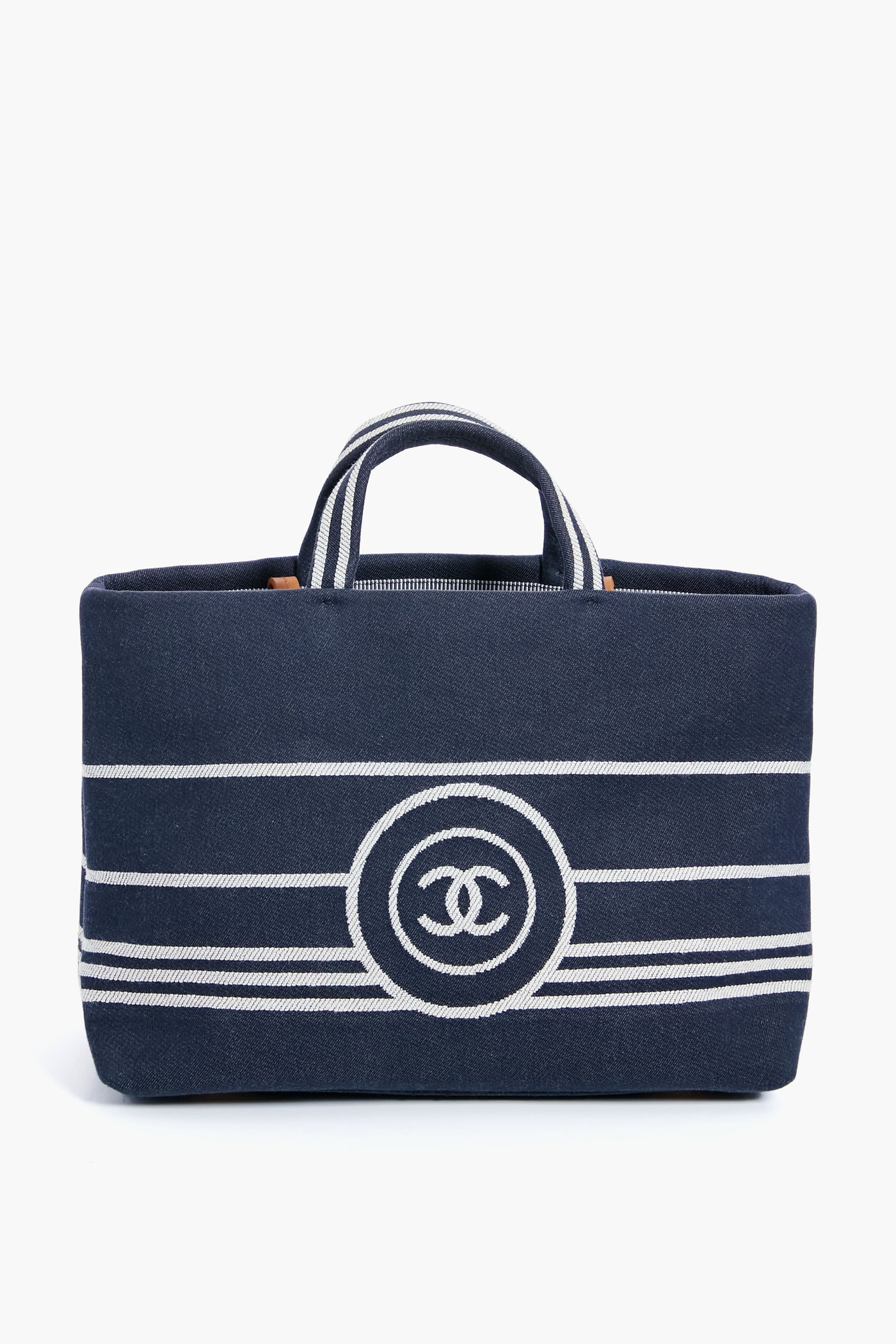 A navy blue luxury handbag with white horizontal stripes, two short handles, and a bold front logo from the Tuckernuck Archive Collection, inspired by the Chanel Denim Canvas Border Tote.