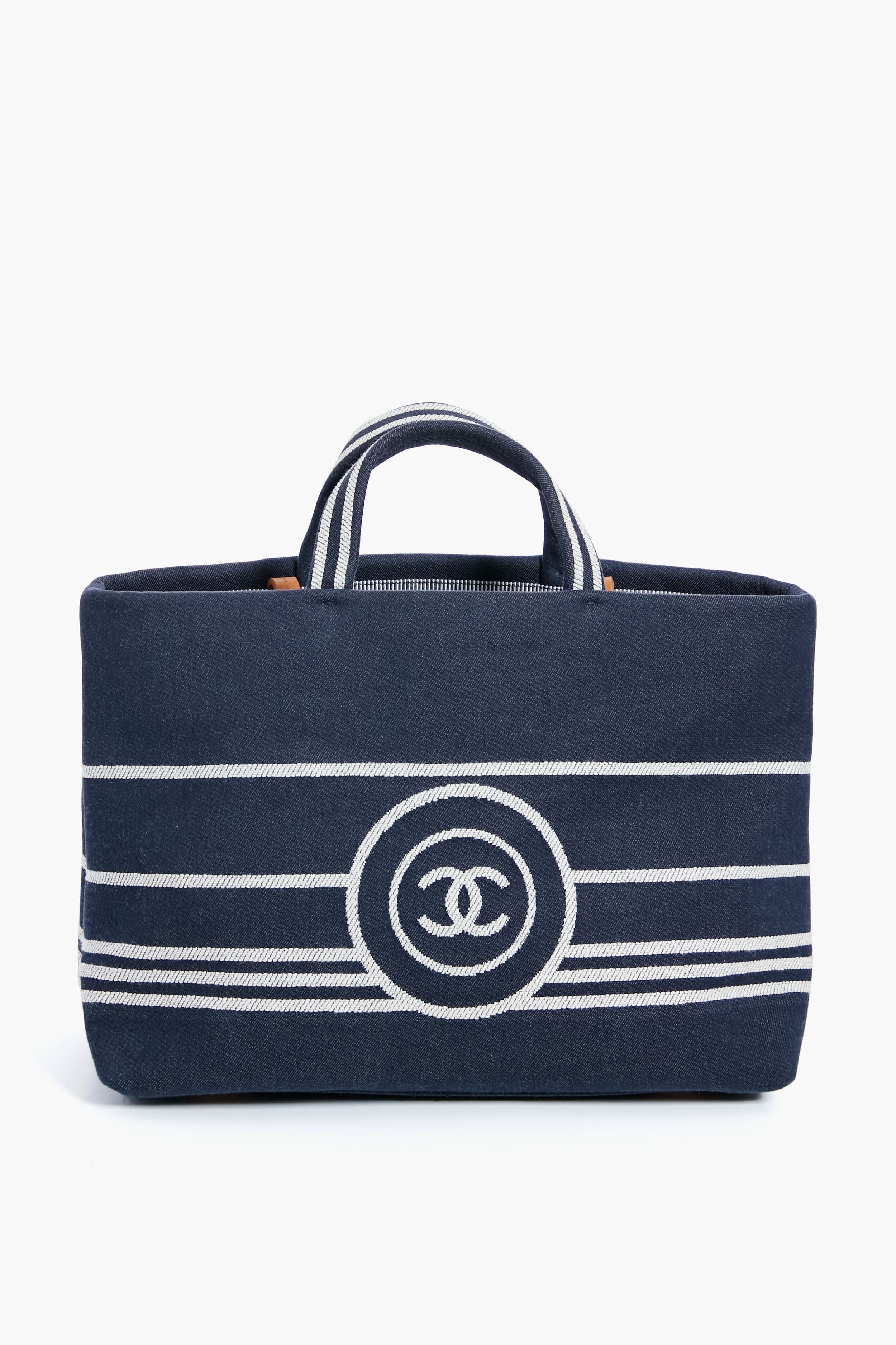 A navy blue luxury handbag with white horizontal stripes, two short handles, and a bold front logo from the Tuckernuck Archive Collection, inspired by the Chanel Denim Canvas Border Tote.