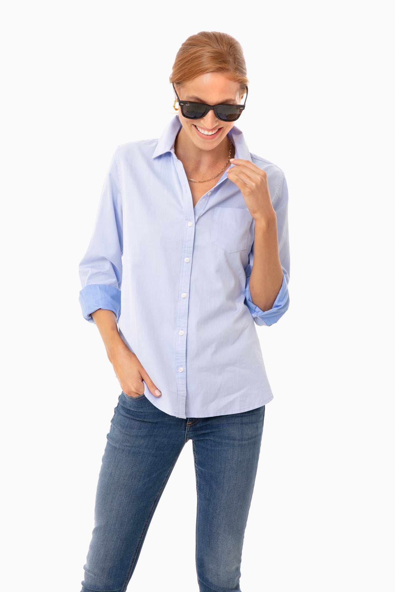 A woman in a light blue TROVATA Birds of Paradis Grace Classic Shirt, blue jeans, and sunglasses stands smiling with one hand in her pocket.