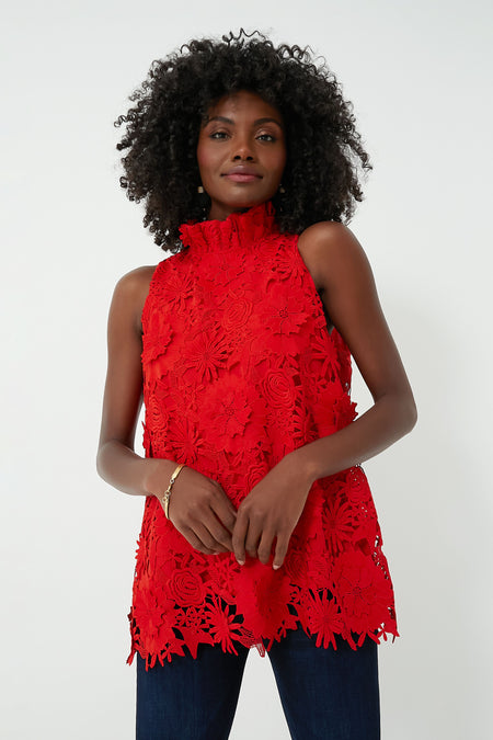 A woman wears a Tuckernuck sleeveless red lace top with floral patterns and a ruffle stand collar, styled with dark blue jeans.