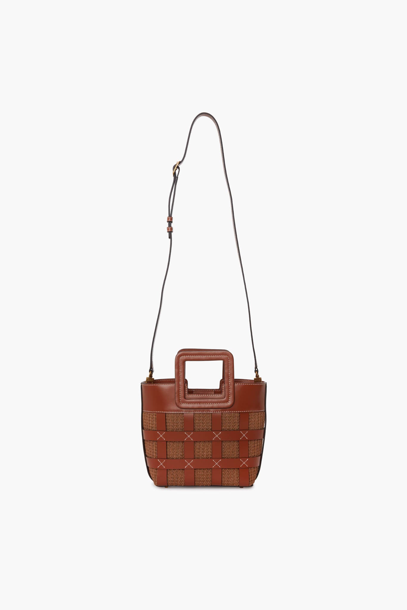 The STAUD Mini Shirley Bag is a small brown designer handbag made of woven leather with a square handle cutout and an adjustable shoulder strap.
