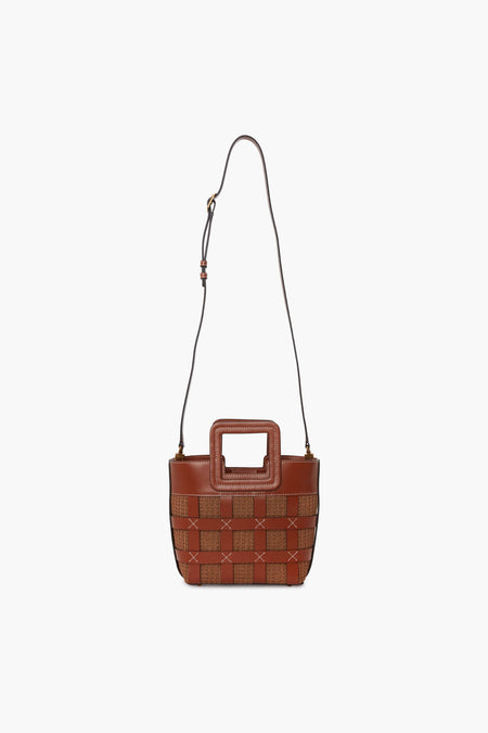 The STAUD Mini Shirley Bag is a small brown designer handbag made of woven leather with a square handle cutout and an adjustable shoulder strap.