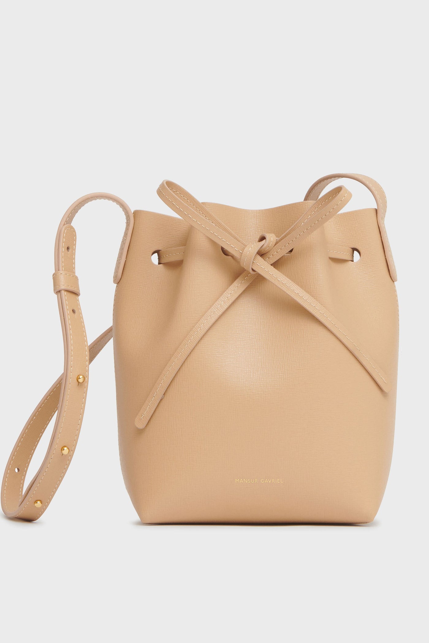 A beige Italian leather bucket bag by Mansur Gavriel features a drawstring closure and an adjustable shoulder strap.