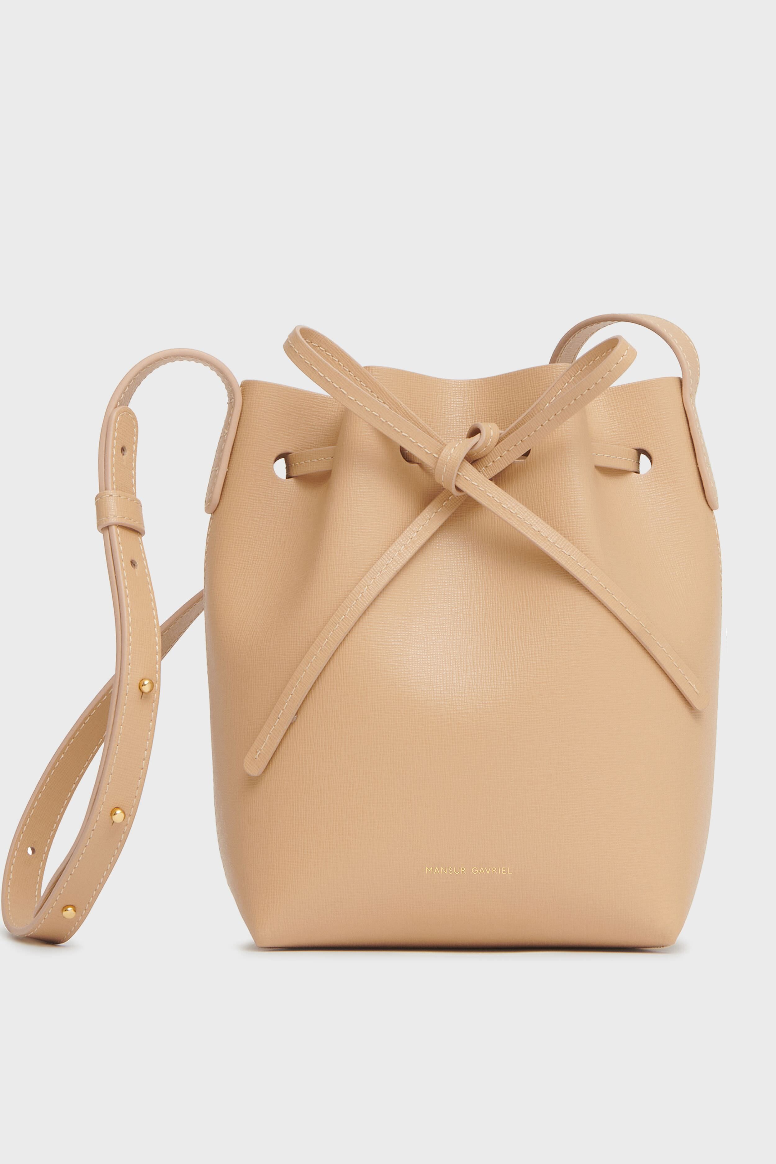 A beige Italian leather bucket bag by Mansur Gavriel features a drawstring closure and an adjustable shoulder strap.