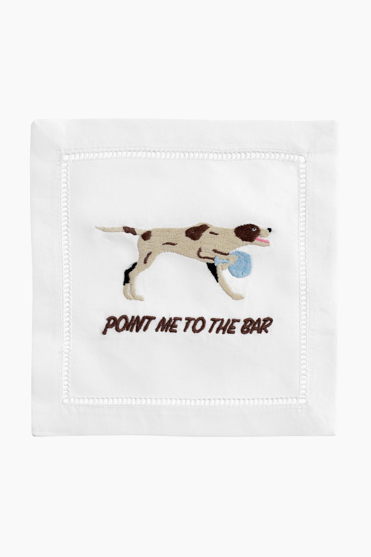 An August Morgan white cocktail napkin features an embroidered brown and white dog with a blue ball and "POINT ME TO THE BAR" stitched below—perfect for entertaining or as a fun hostess gift.