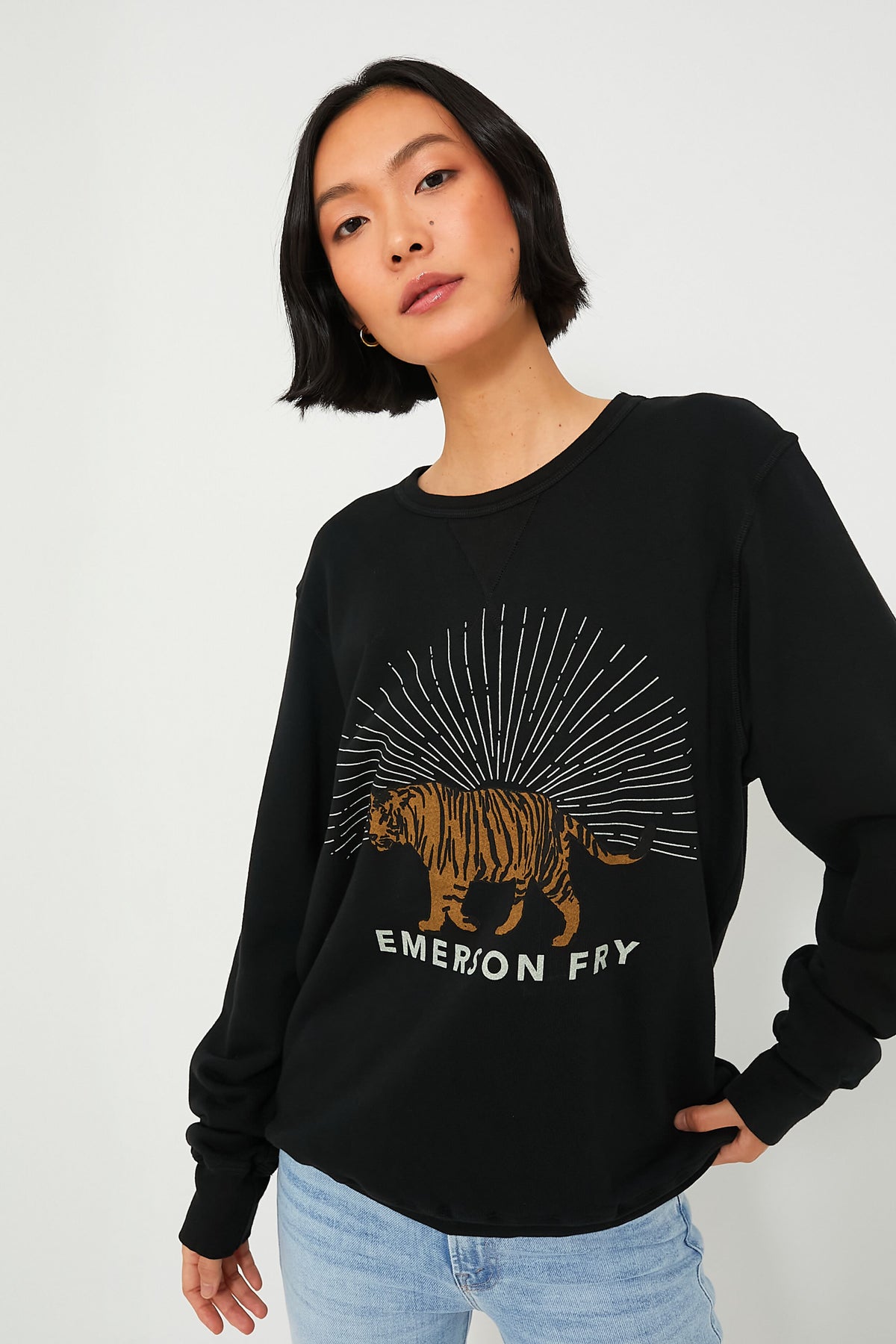 A woman with short black hair wears an Emerson Fry French terry Tiger Sweatshirt, paired with light blue jeans.