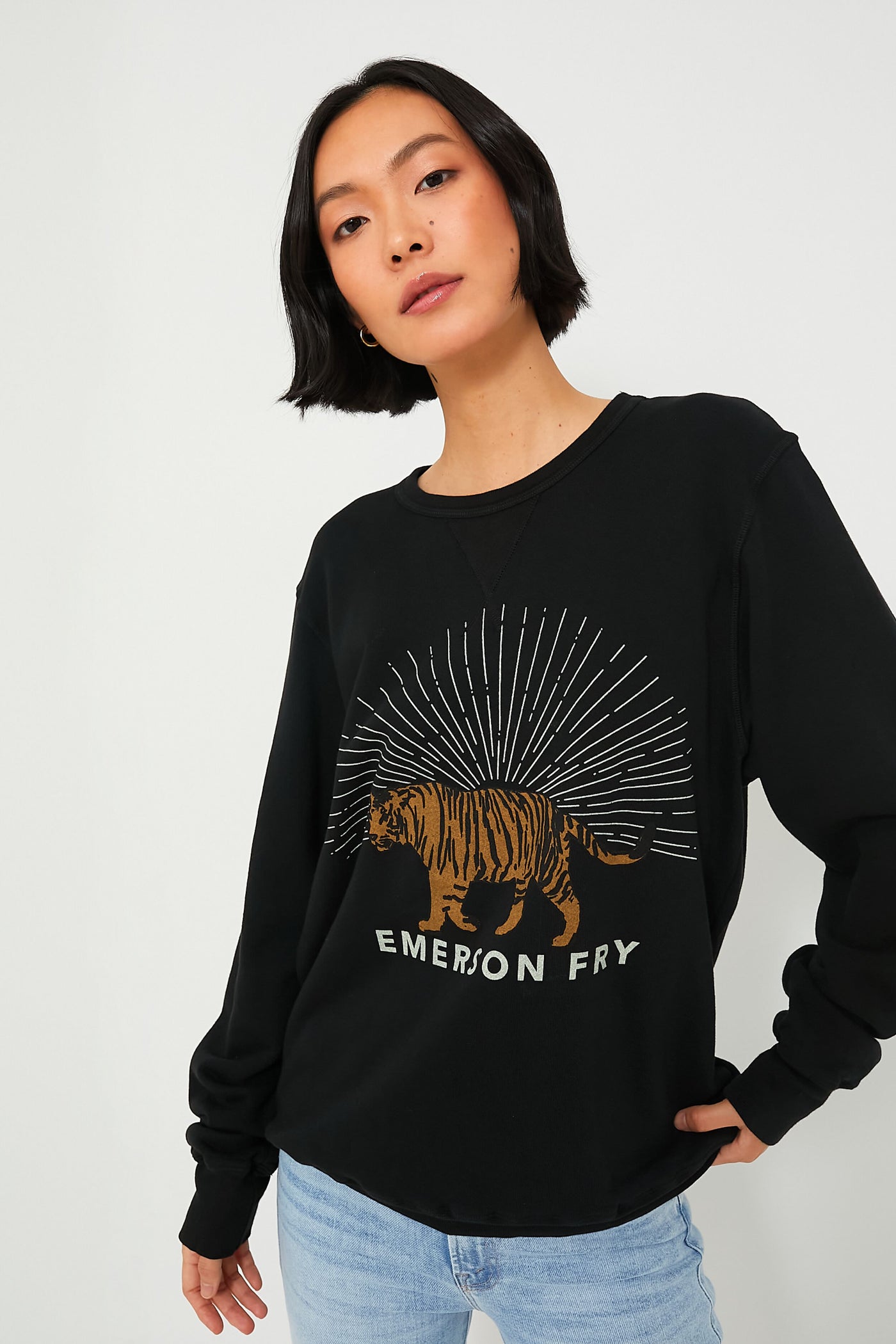 A woman with short black hair wears an Emerson Fry French terry Tiger Sweatshirt, paired with light blue jeans.
