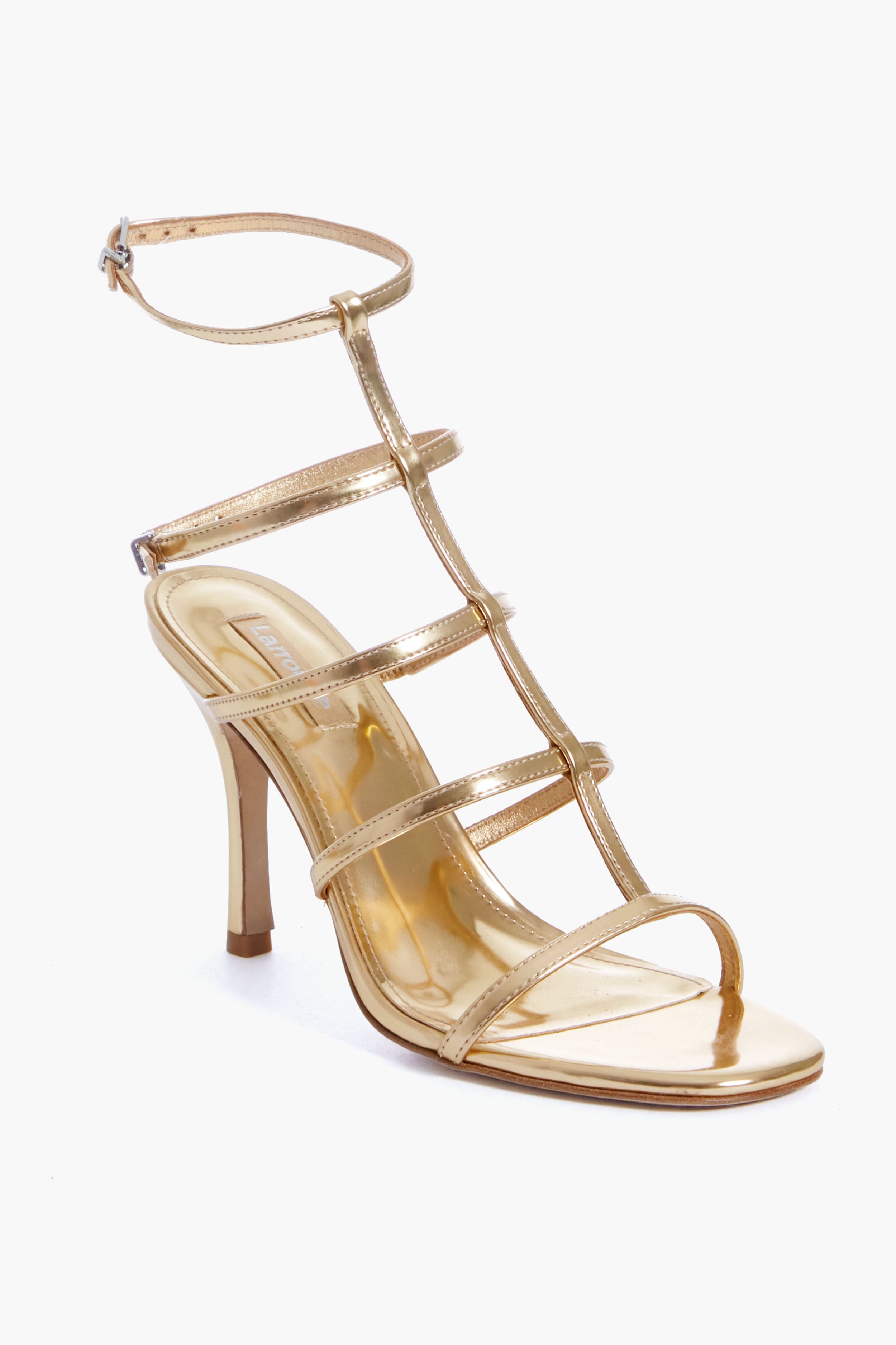 The Larroude Gold Specchio Serena Sandals are gold high-heeled sandals featuring multiple thin straps and an ankle buckle, making a bold statement as metallic strappy heels.