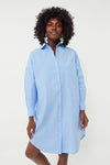 A woman wears the LMND Chiara Shirt Dress in light blue cotton poplin with an oversized fit, styled with large silver earrings.