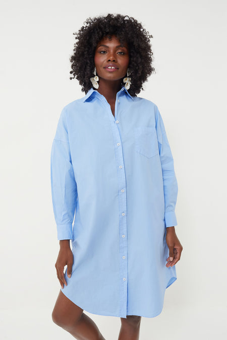 A woman wears the LMND Chiara Shirt Dress in light blue cotton poplin with an oversized fit, styled with large silver earrings.
