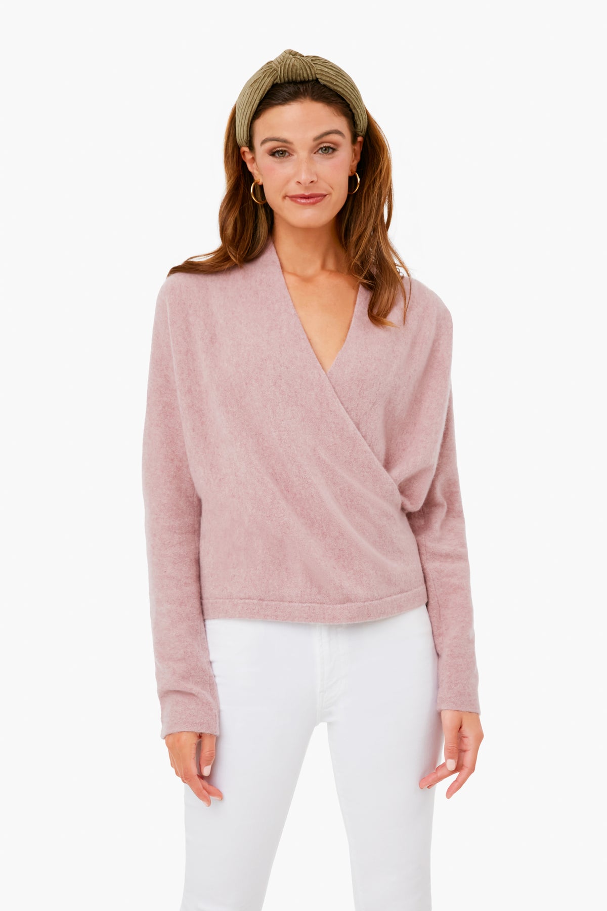 A woman wears a Vince light pink boiled cashmere wrap-front pullover, white pants, and an olive green headband.