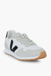 A VEJA sneaker in white and light gray, featuring a black V logo, beige vegan suede details, and a gum rubber sole.