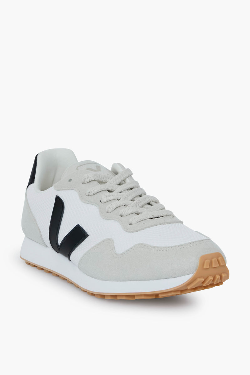A VEJA sneaker in white and light gray, featuring a black V logo, beige vegan suede details, and a gum rubber sole.