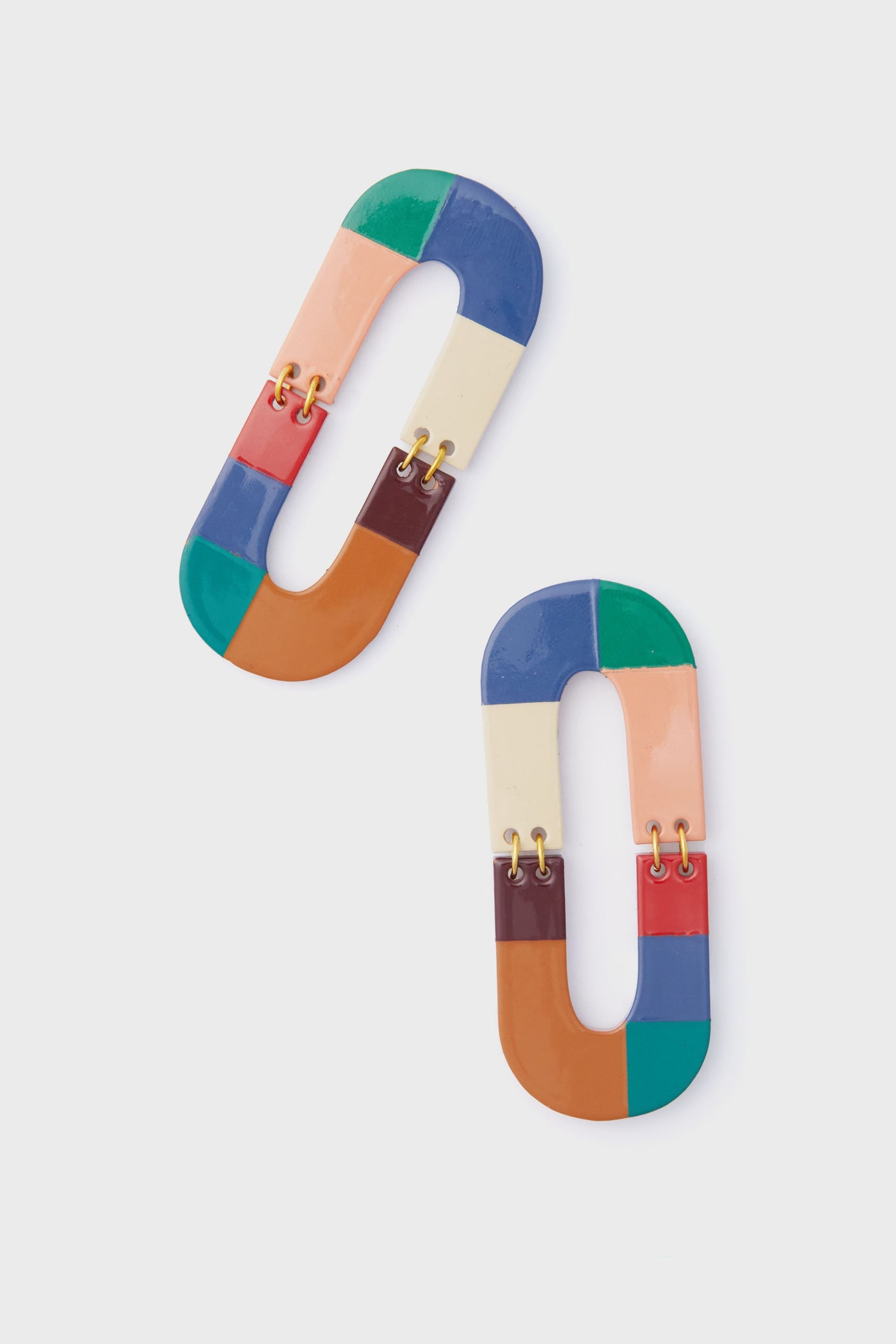 Sunshine Tienda’s boho-chic earrings feature two oval shapes with multicolored segments, connected by small gold links and crafted in a vibrant hand-painted jewelry style.