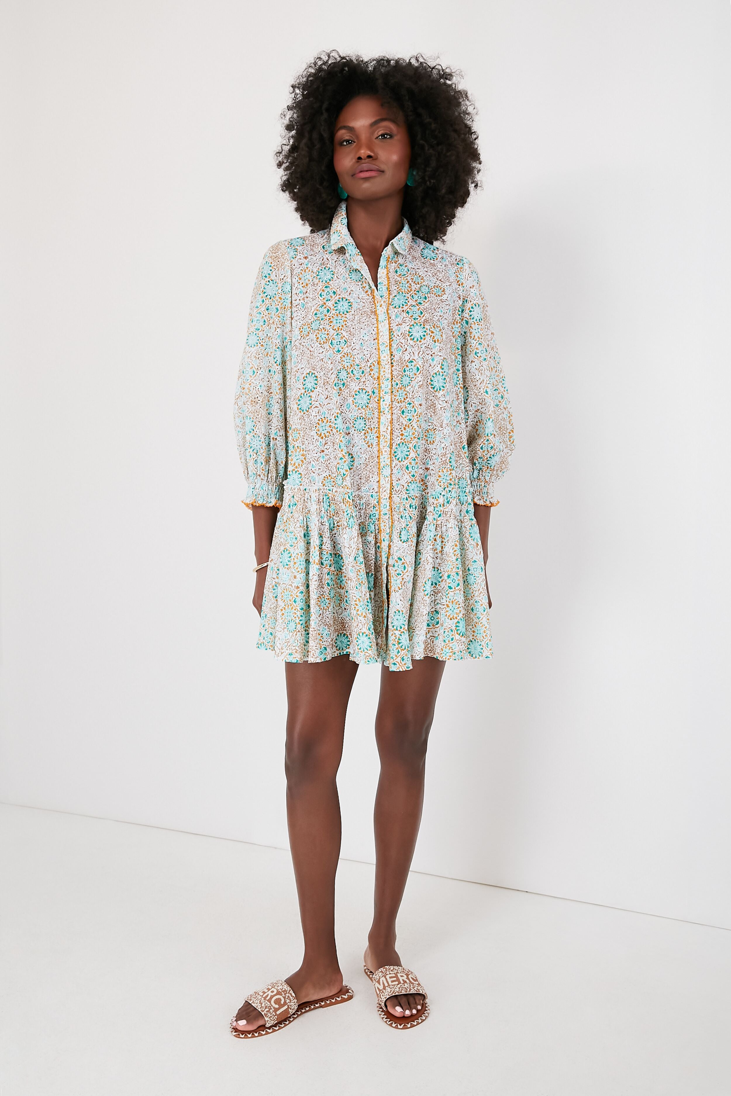 Woman in a Poupette St Barth floral long-sleeve shirtdress with a collar, paired with flat sandals for an effortless, boho-chic look.