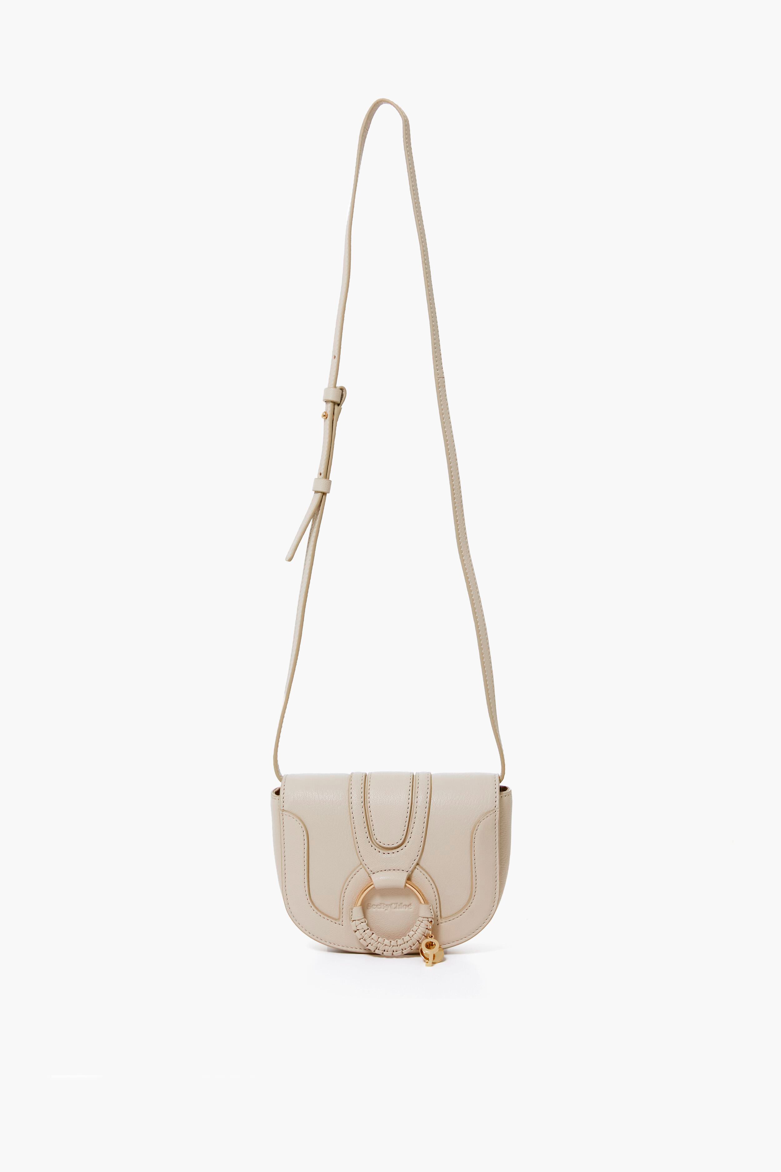 A small beige See by Chloe Mini Hana Bag featuring an adjustable strap, flap closure, and signature front ring detail—a stylish goatskin designer crossbody ideal for any occasion.