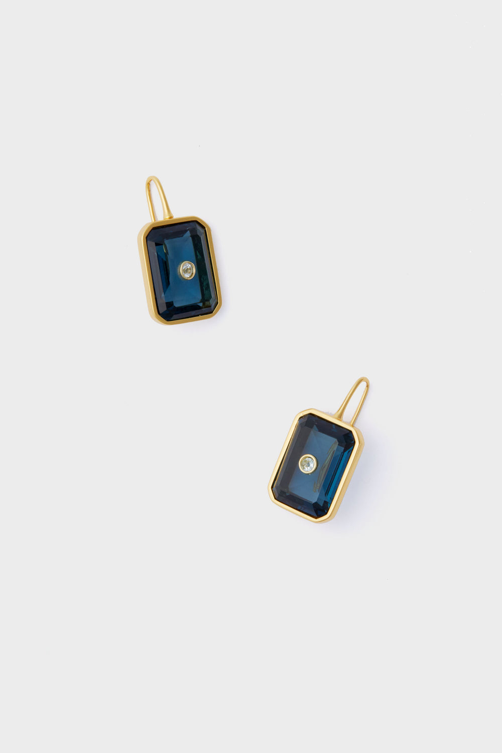 A pair of rectangular gold Denim Tile Earrings by Lizzie Fortunato, featuring dark blue stones and a central clear gemstone—perfect for fans of unique jewelry.