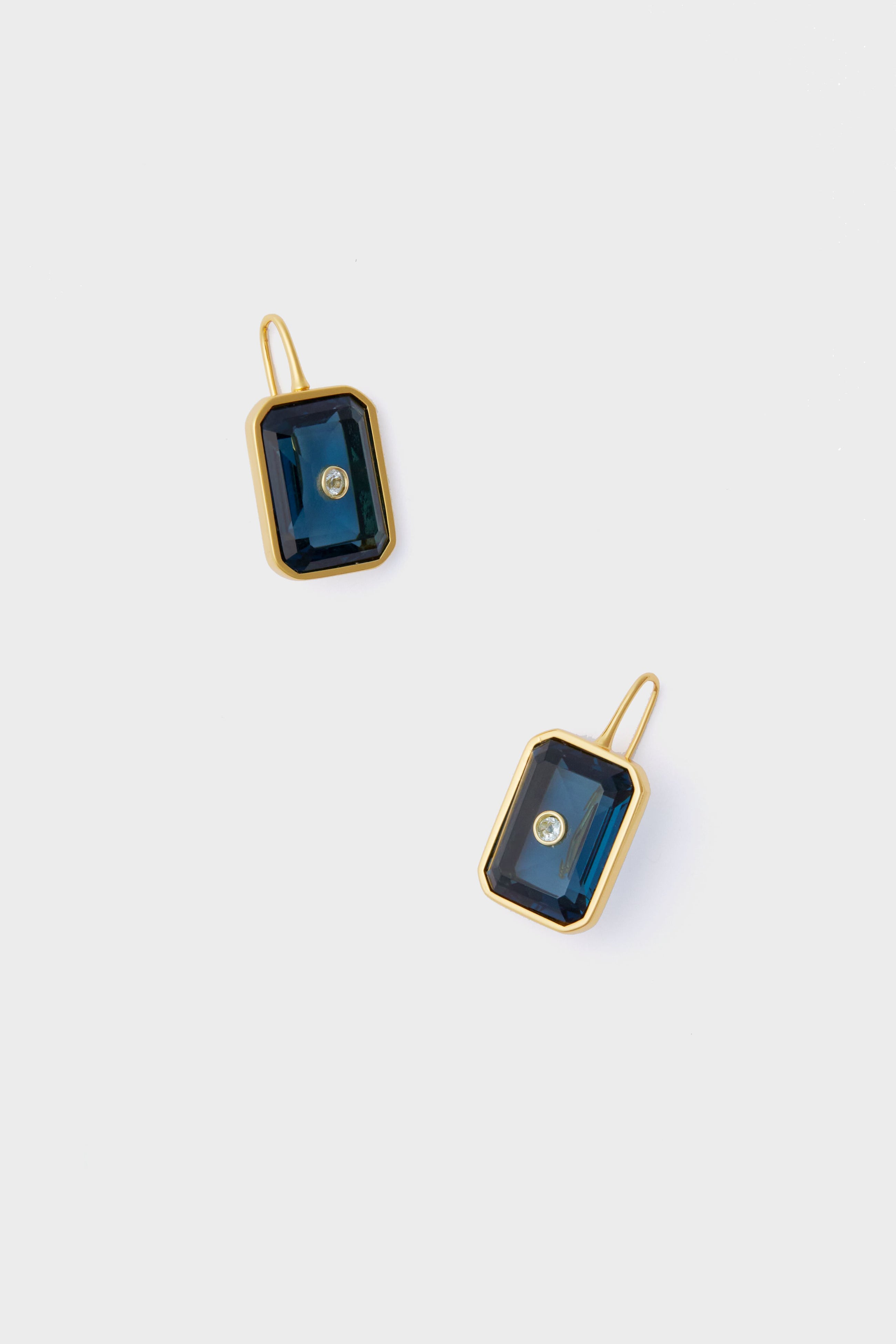 A pair of rectangular gold Denim Tile Earrings by Lizzie Fortunato, featuring dark blue stones and a central clear gemstone—perfect for fans of unique jewelry.