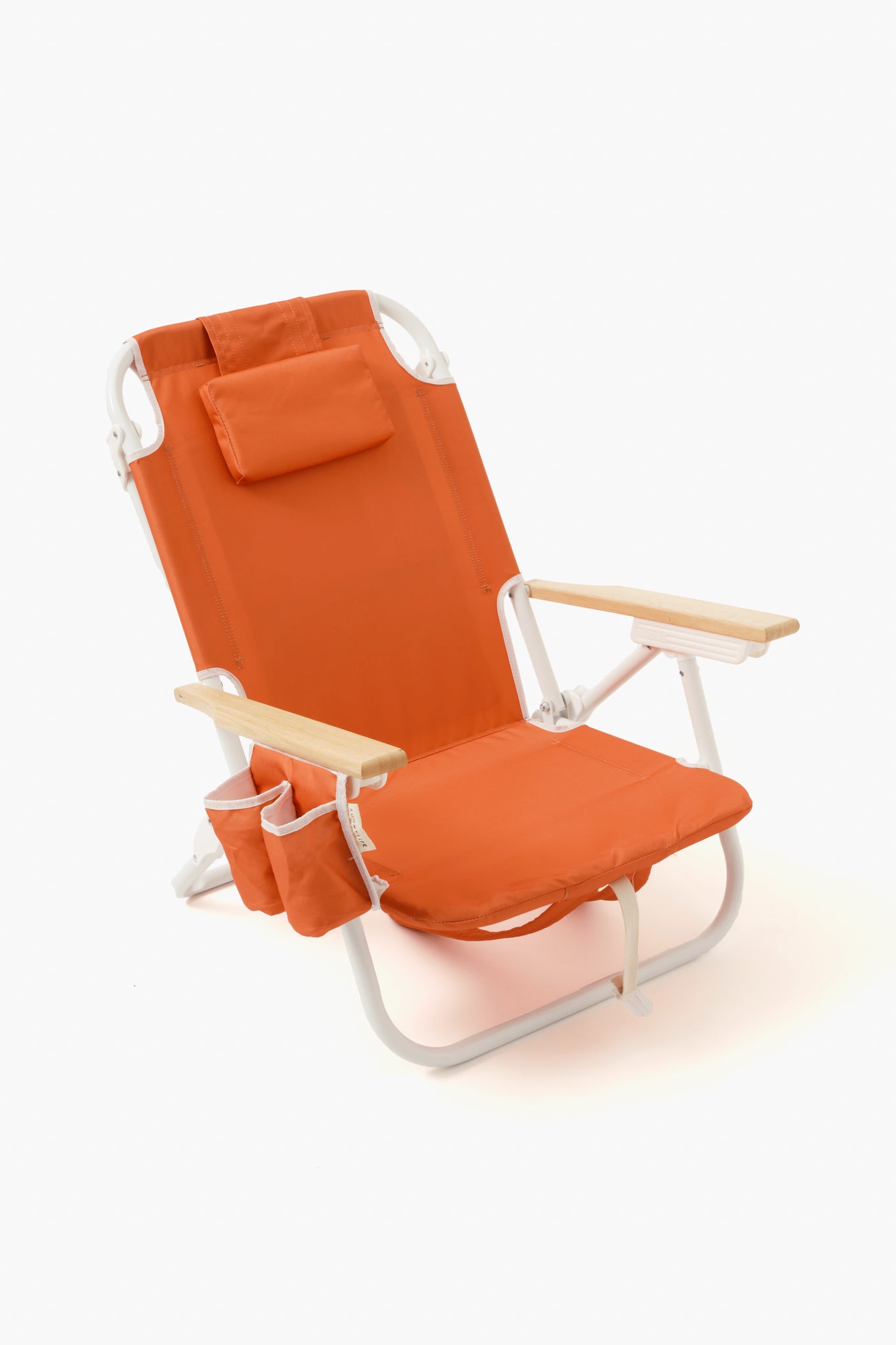 The Sunnylife deluxe orange beach chair features a headrest, wooden armrests, side pockets, a drink holder, and a white metal frame—offering comfort and convenience for your seaside days.