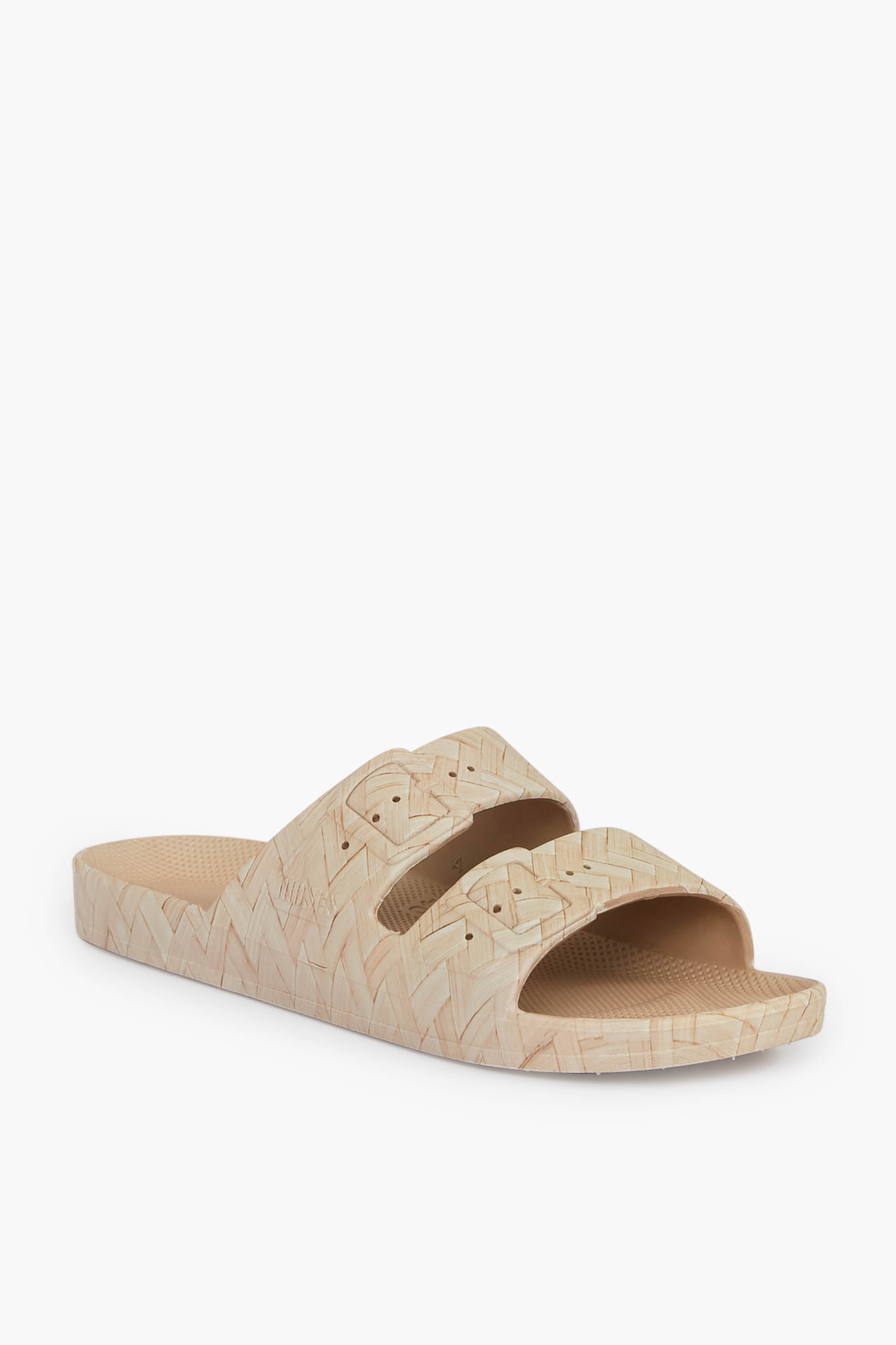 The Freedom Moses beige sandal features two wide straps with a textured, woven pattern on both the straps and sole. This stylish vegan sandal offers a sustainable footwear choice for eco-conscious shoppers.