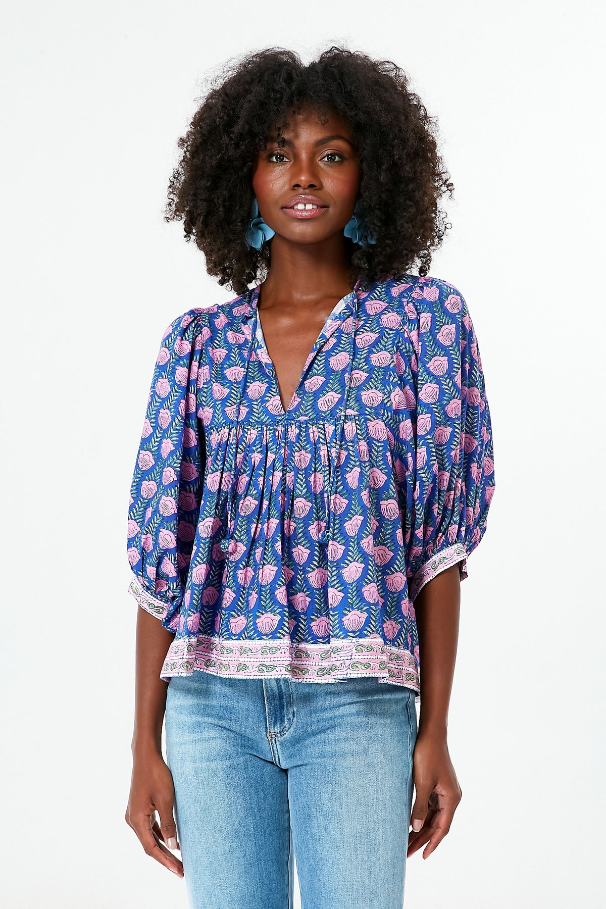 A woman models the Saylor boho blouse featuring blue and pink block print, a V-neckline, and a relaxed fit, paired with light blue jeans.