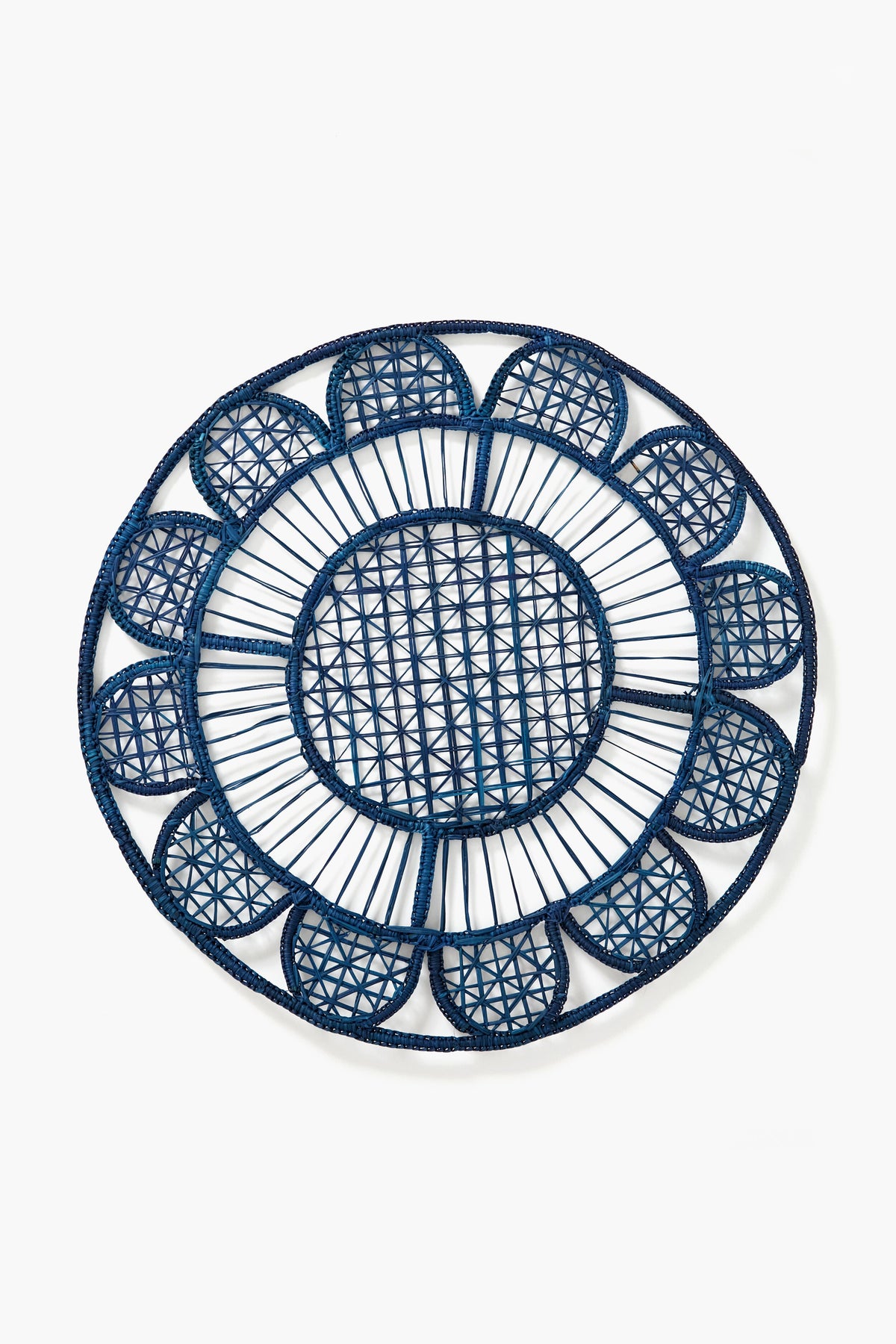 The Coro Cora round handmade placemat, in navy blue with a geometric and scalloped edge design, is crafted from natural fibers to add artisan style to your table.