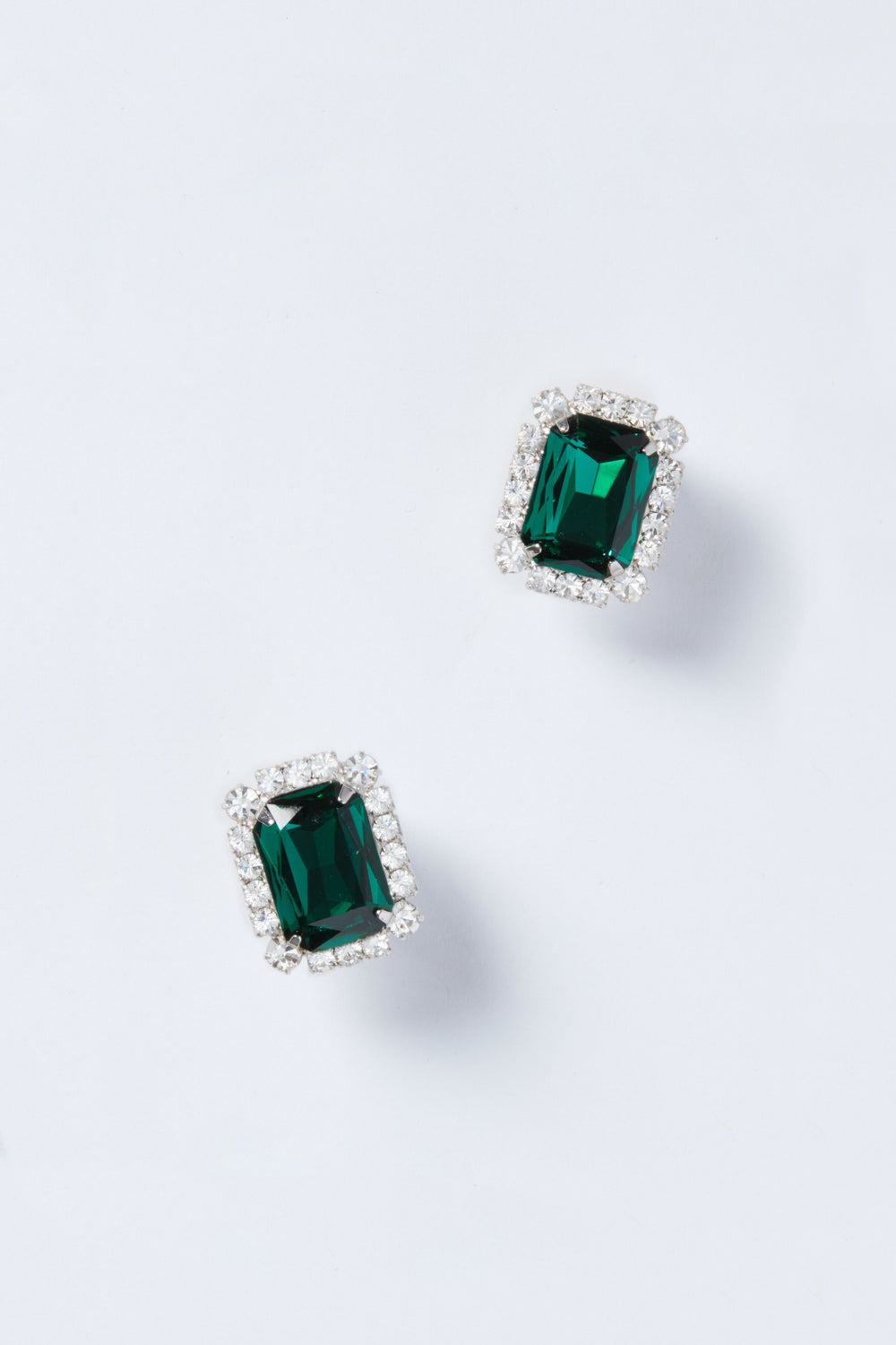 Jennifer Behr’s rectangular emerald stud earrings, each bordered with sparkling clear stones, highlight the elegance of luxury accessories.