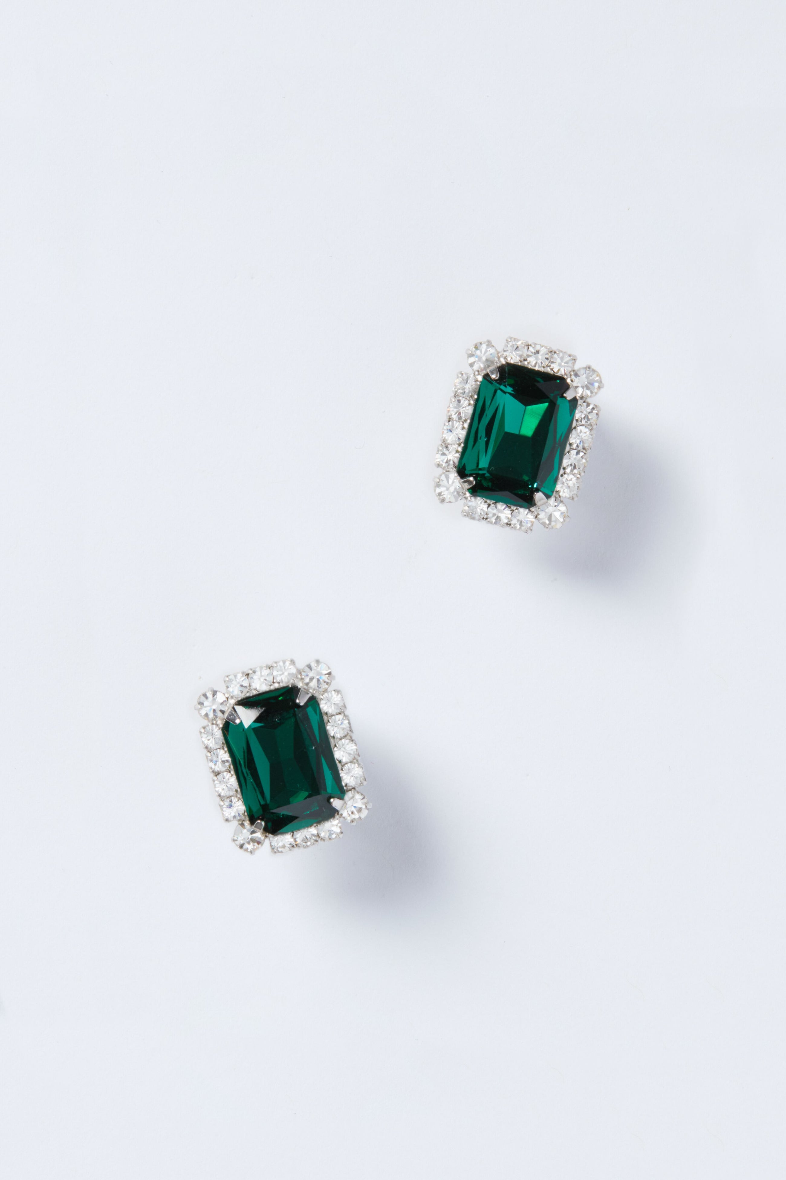 Jennifer Behr’s rectangular emerald stud earrings, each bordered with sparkling clear stones, highlight the elegance of luxury accessories.