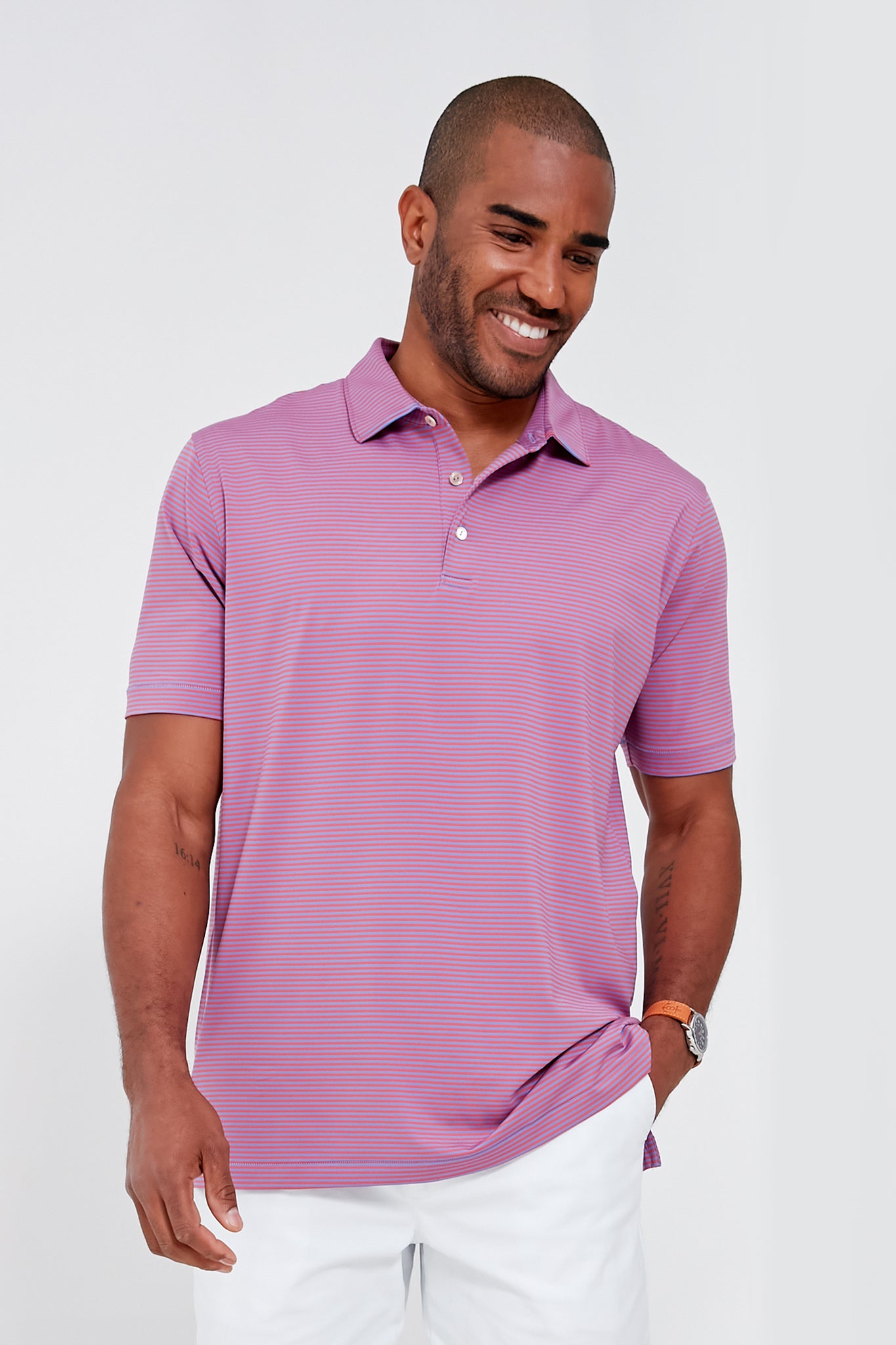 A man in a Peter Millar light purple moisture-wicking performance polo and white pants stands smiling as he looks down.