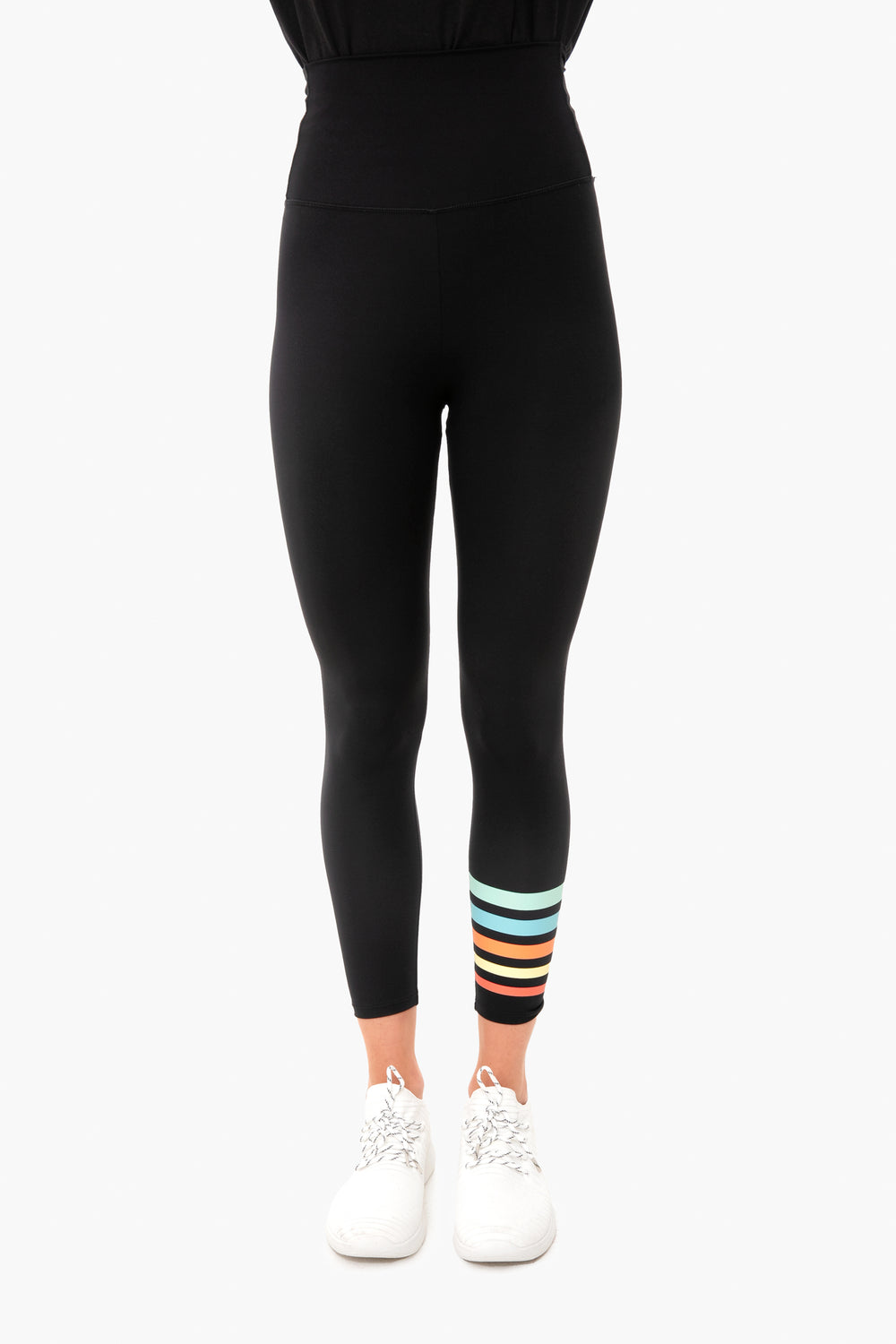 Person in Addison Bay black high-waisted leggings with colorful horizontal stripes near the left ankle and white athletic shoes. These Everyday Leggings offer sweat-wicking fabric and a high-rise waist for all-day comfort.