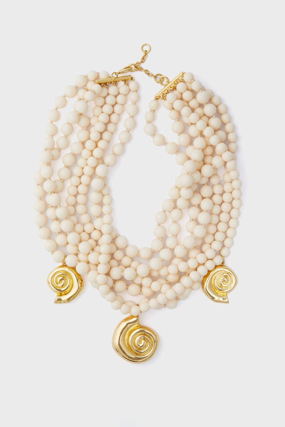 Tuckernuck Jewelry multi-strand cream beaded statement necklace with three gold shell pendants and a gold clasp.