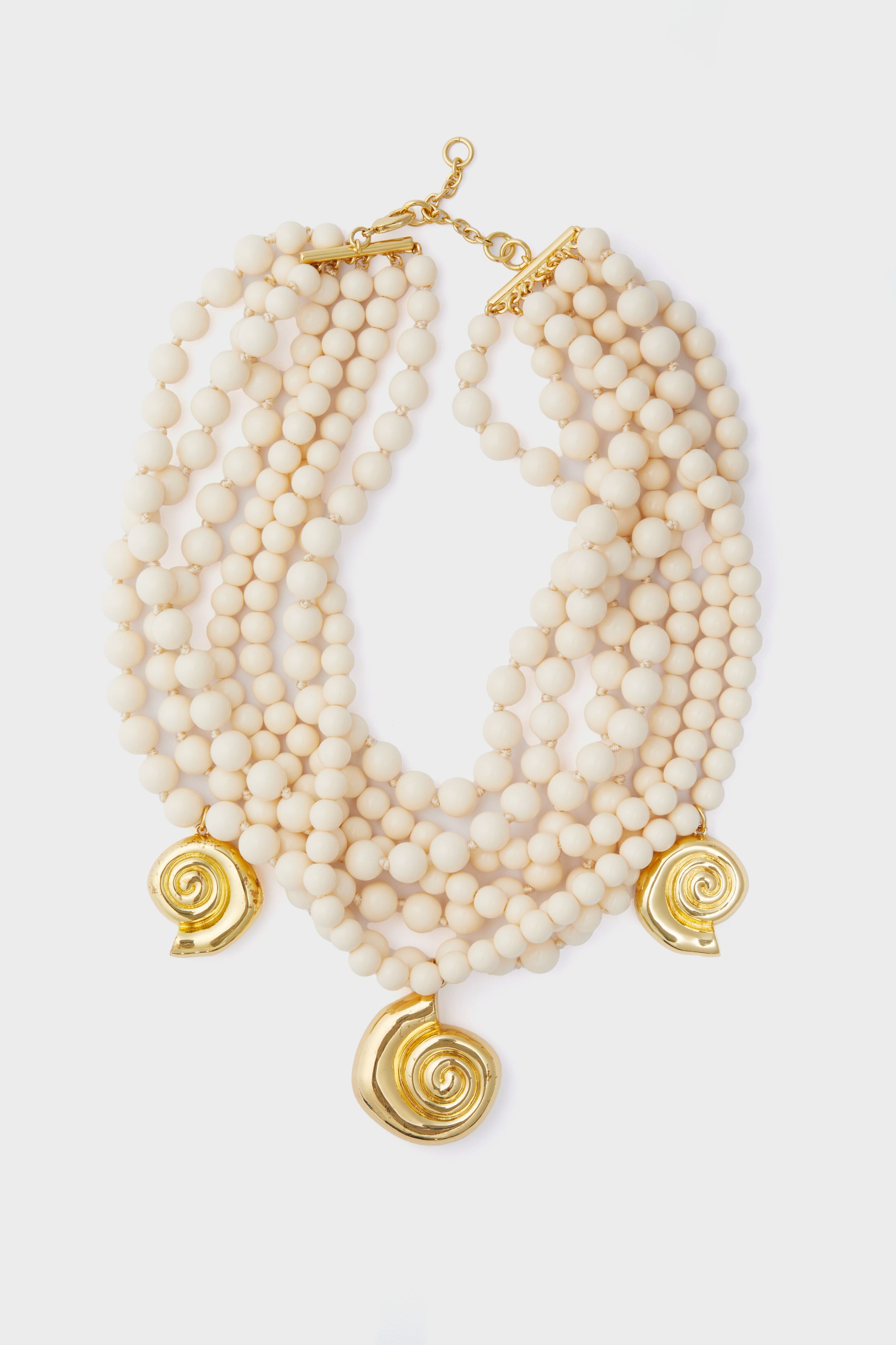 Tuckernuck Jewelry multi-strand cream beaded statement necklace with three gold shell pendants and a gold clasp.