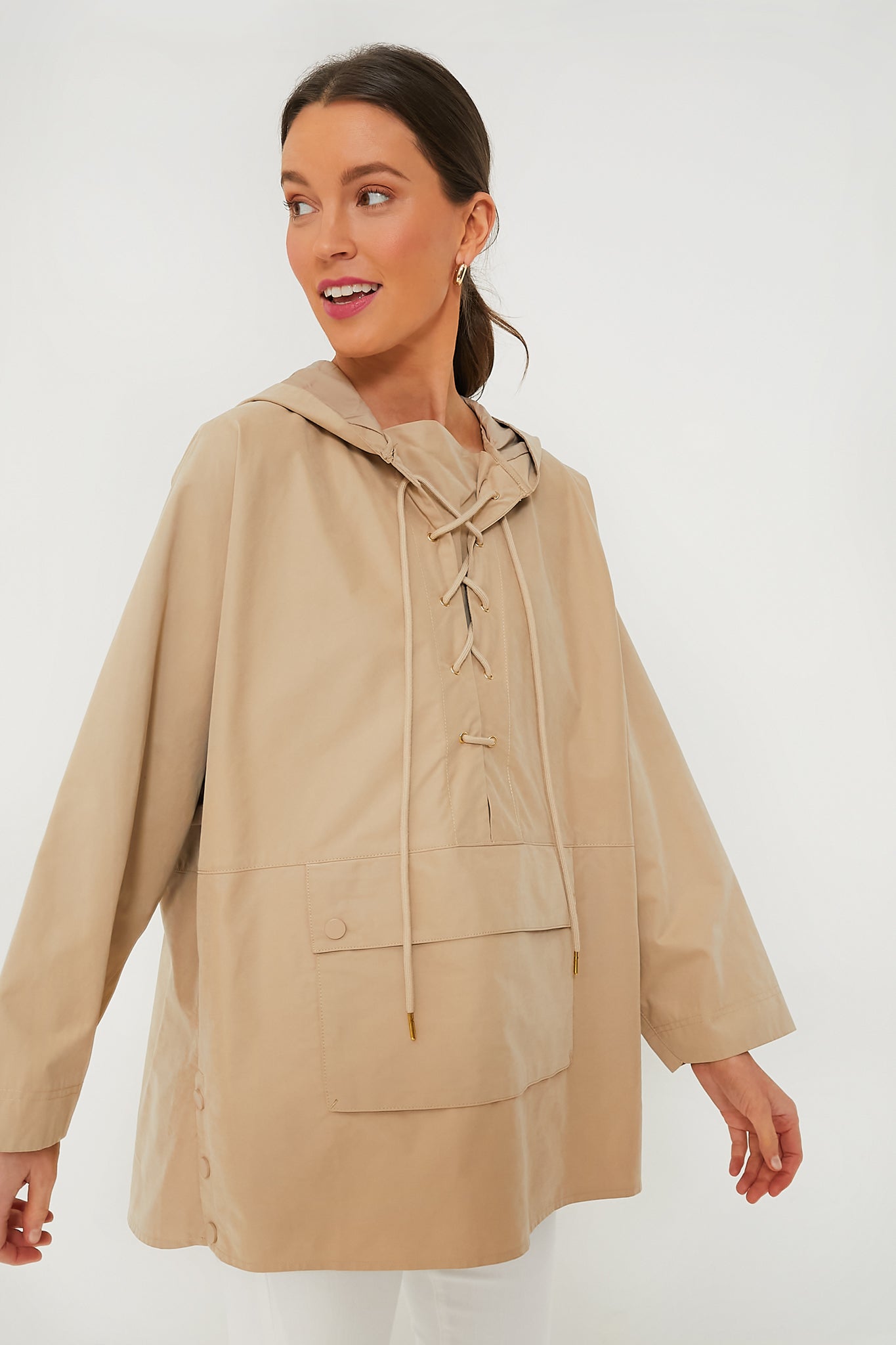 A woman wears a Pomander Place Beige Sterling Pullover, a loose-fitting, lightweight hoodie with a lace-up front and front pocket.
