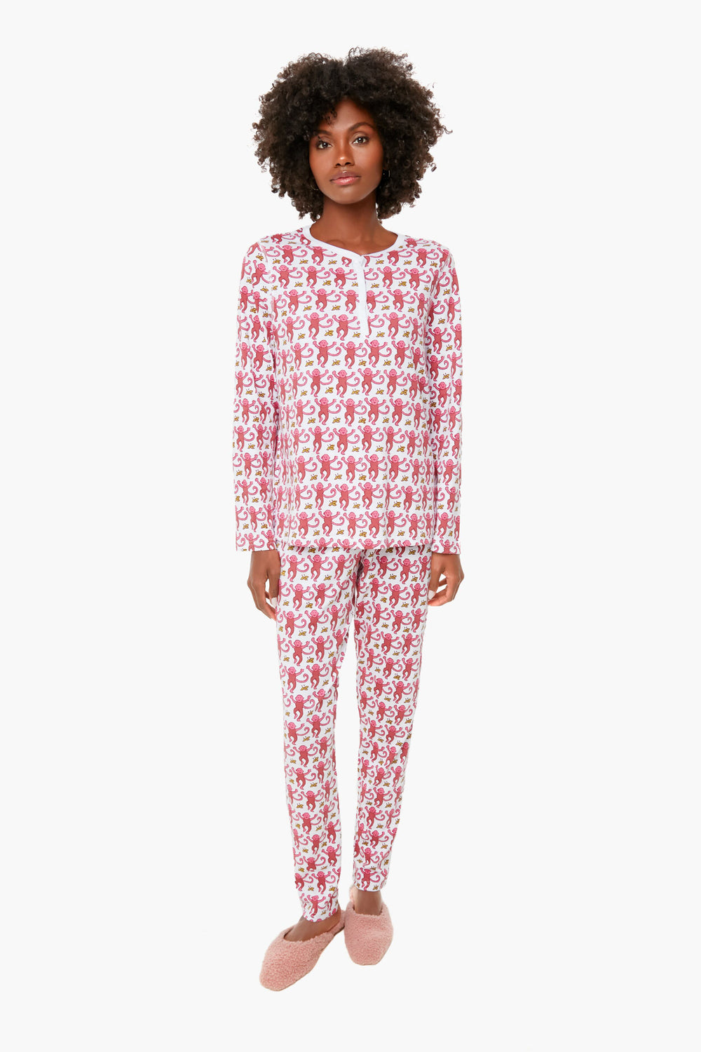 A woman wears Roller Rabbit's Pink Monkey Pajamas, a matching cotton set with a red and white cartoon print, paired with pink slippers.
