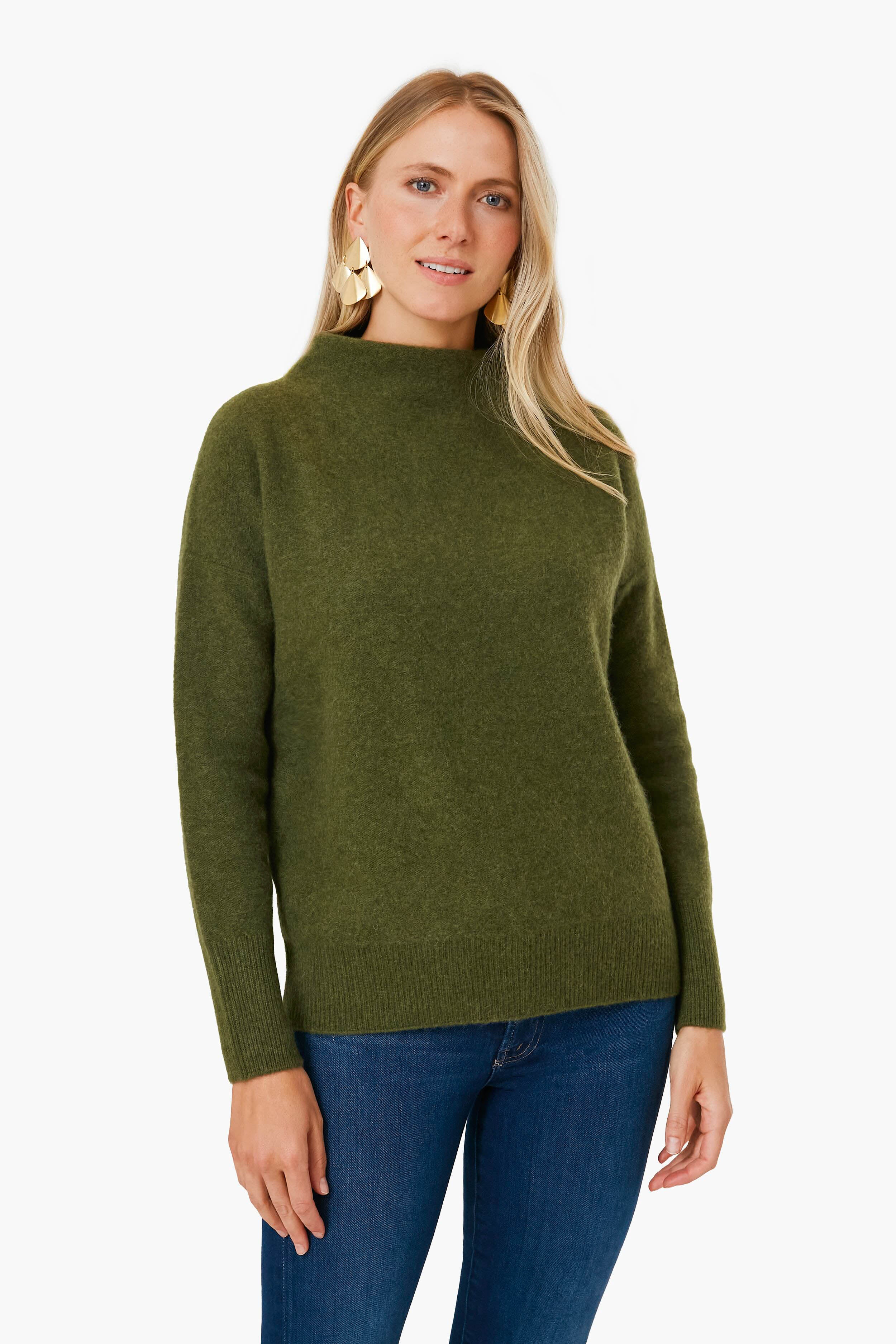 A woman wears a moss green boiled cashmere sweater by Vince—a true luxury wardrobe essential—paired with blue jeans.