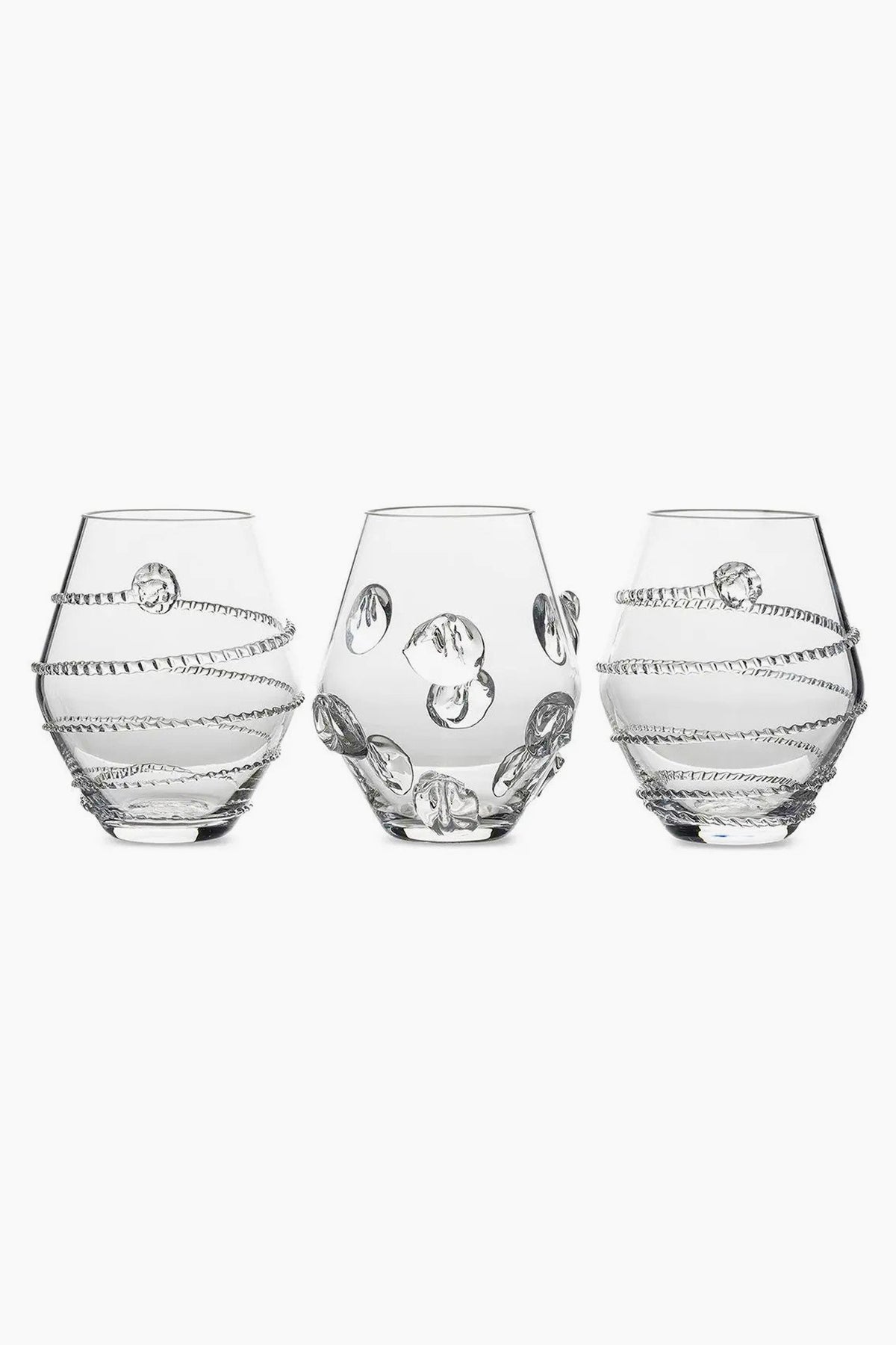 Three clear, round Juliska glasses with decorative raised patterns—two with spiral designs and one with circular accents—are crafted from mouth-blown Czech glass, making them a unique table centerpiece.