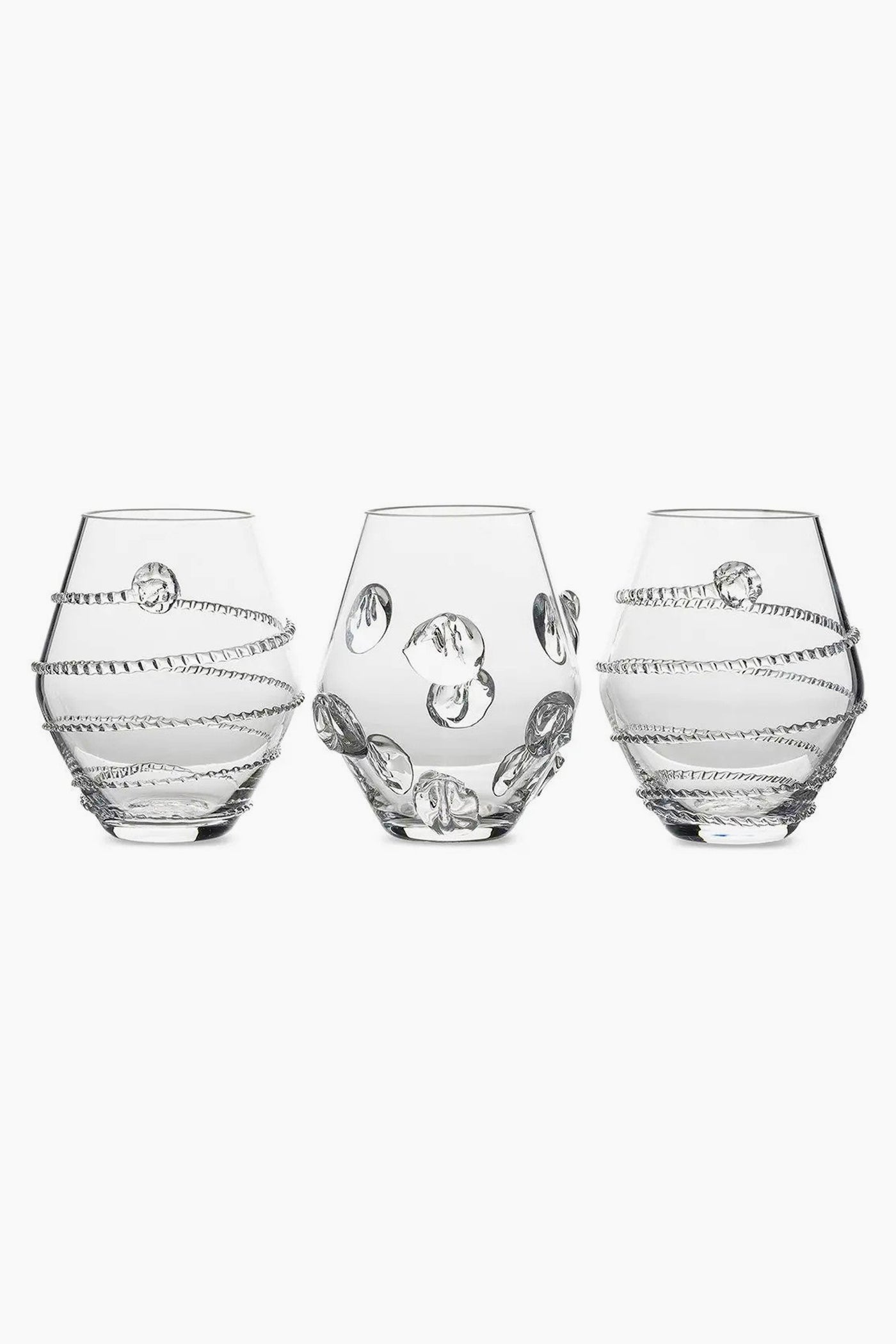 Three clear, round Juliska glasses with decorative raised patterns—two with spiral designs and one with circular accents—are crafted from mouth-blown Czech glass, making them a unique table centerpiece.