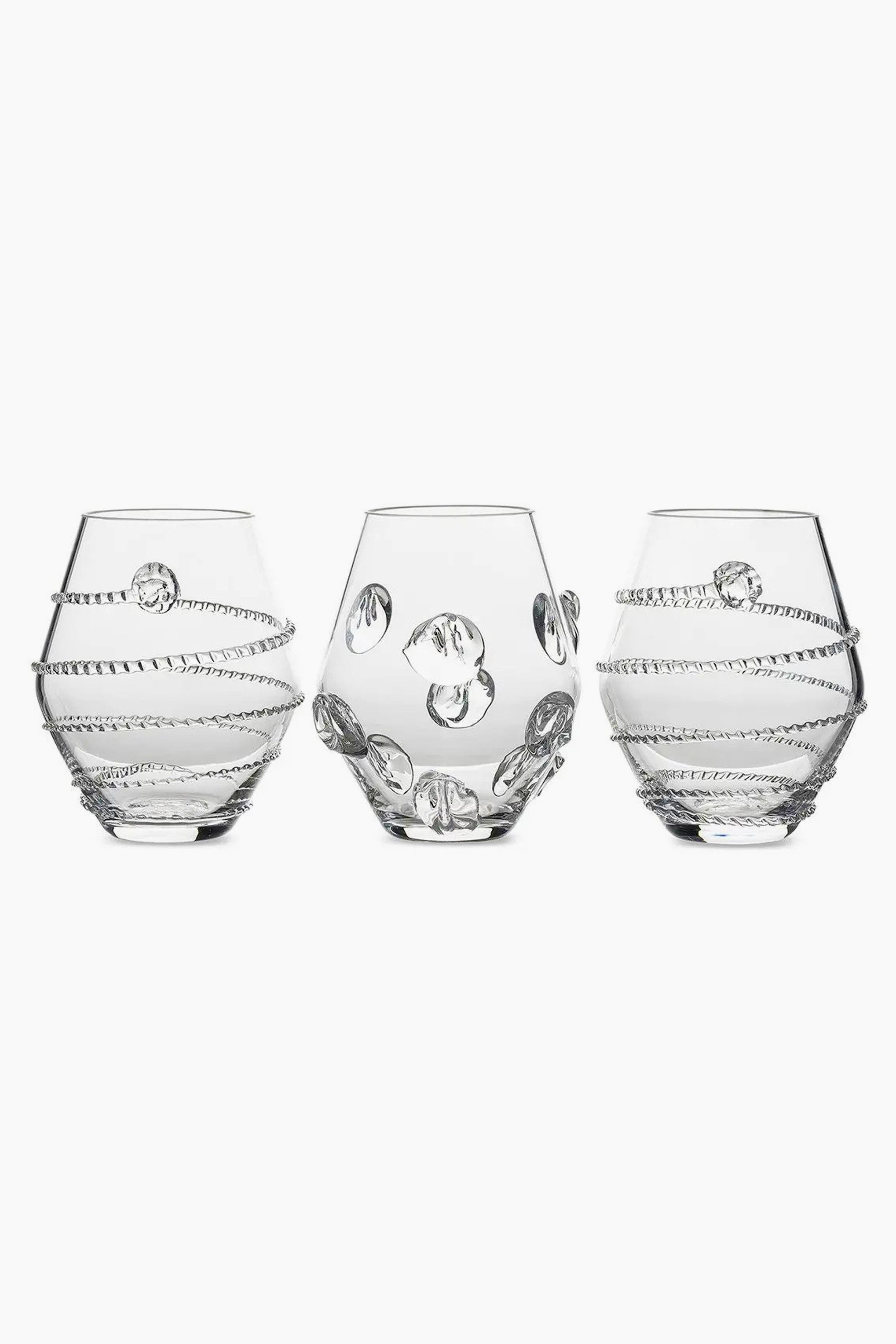 Three clear, round Juliska glasses with decorative raised patterns—two with spiral designs and one with circular accents—are crafted from mouth-blown Czech glass, making them a unique table centerpiece.